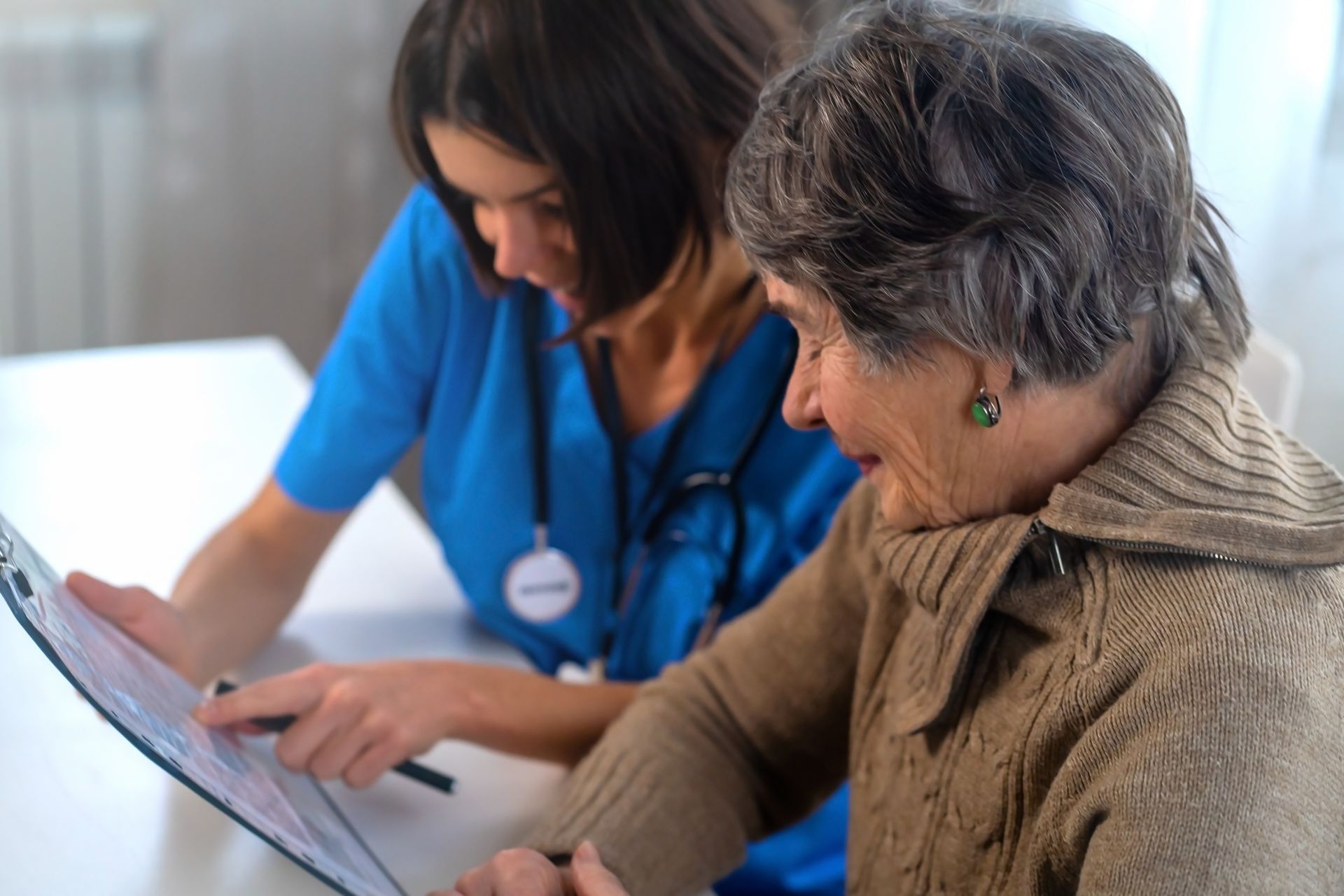 A healthcare professional in blue scrubs points at a document for an older person to review A healthcare professional in blue scrubs points at a document for an older person to review