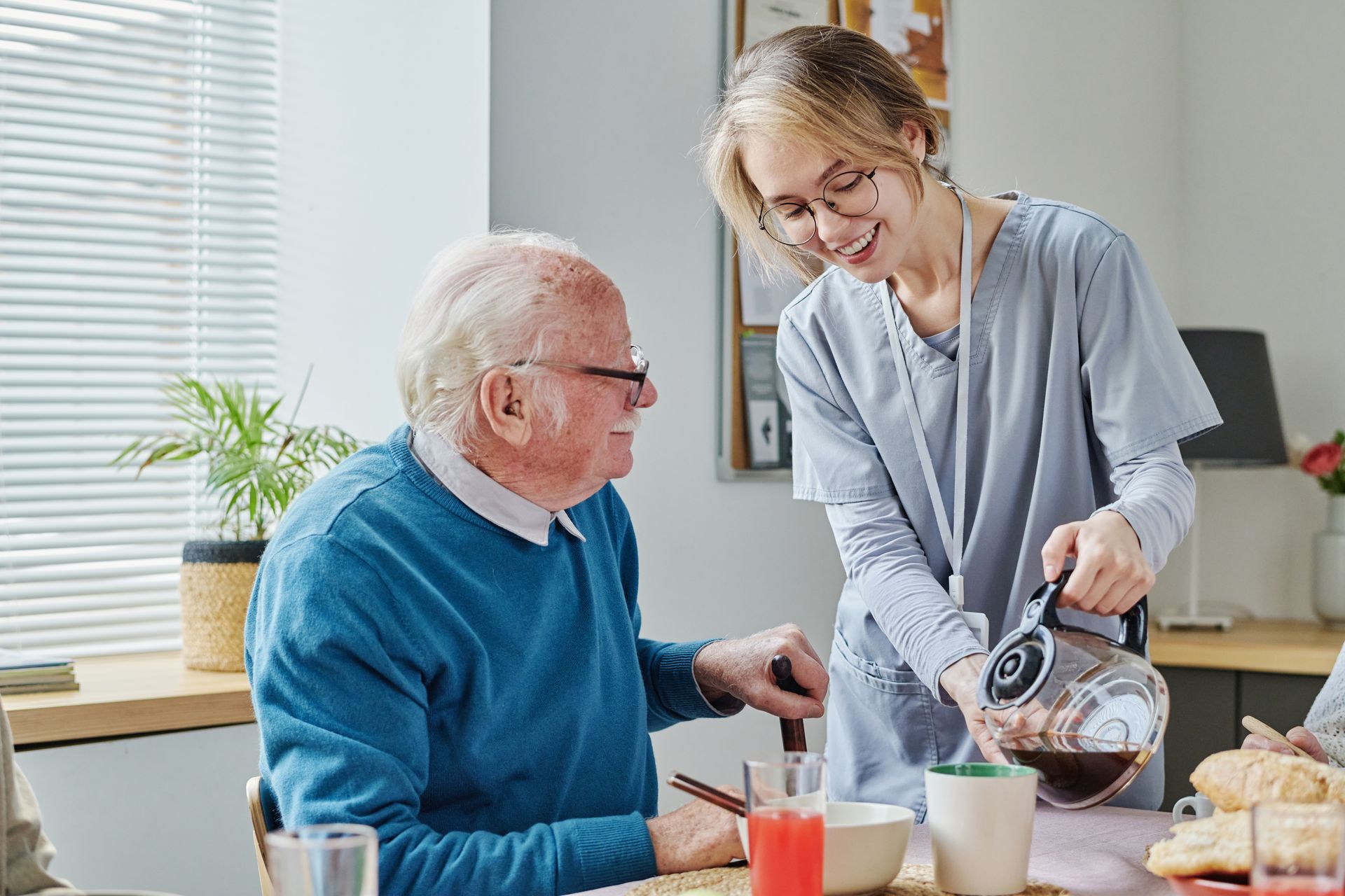 Caregiver pouring coffee for an elderly person at a breakfast table Caregiver pouring coffee for an elderly person at a breakfast table