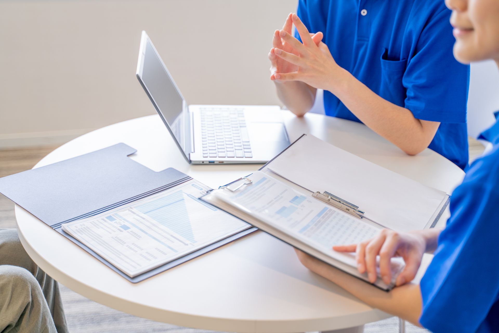 People in blue shirts review documents at a table with a laptop