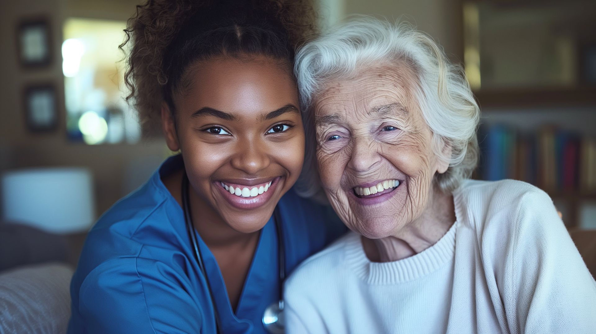Caregiver in blue scrubs smiles at older person on couch, arms around each other. Caregiver in blue scrubs smiles at older person on couch, arms around each other.