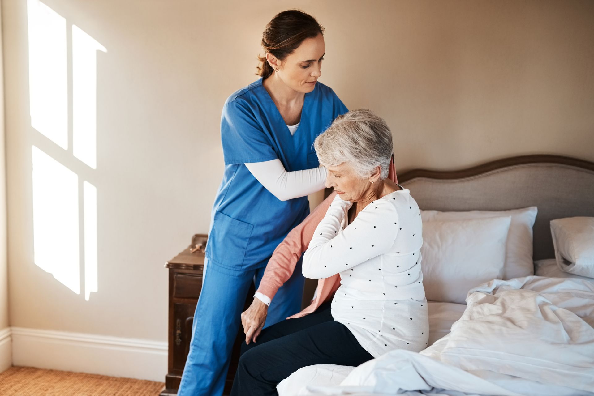 Nurse helping a person sit up in bed; indoors, window, sunlight Nurse helping a person sit up in bed; indoors, window, sunlight