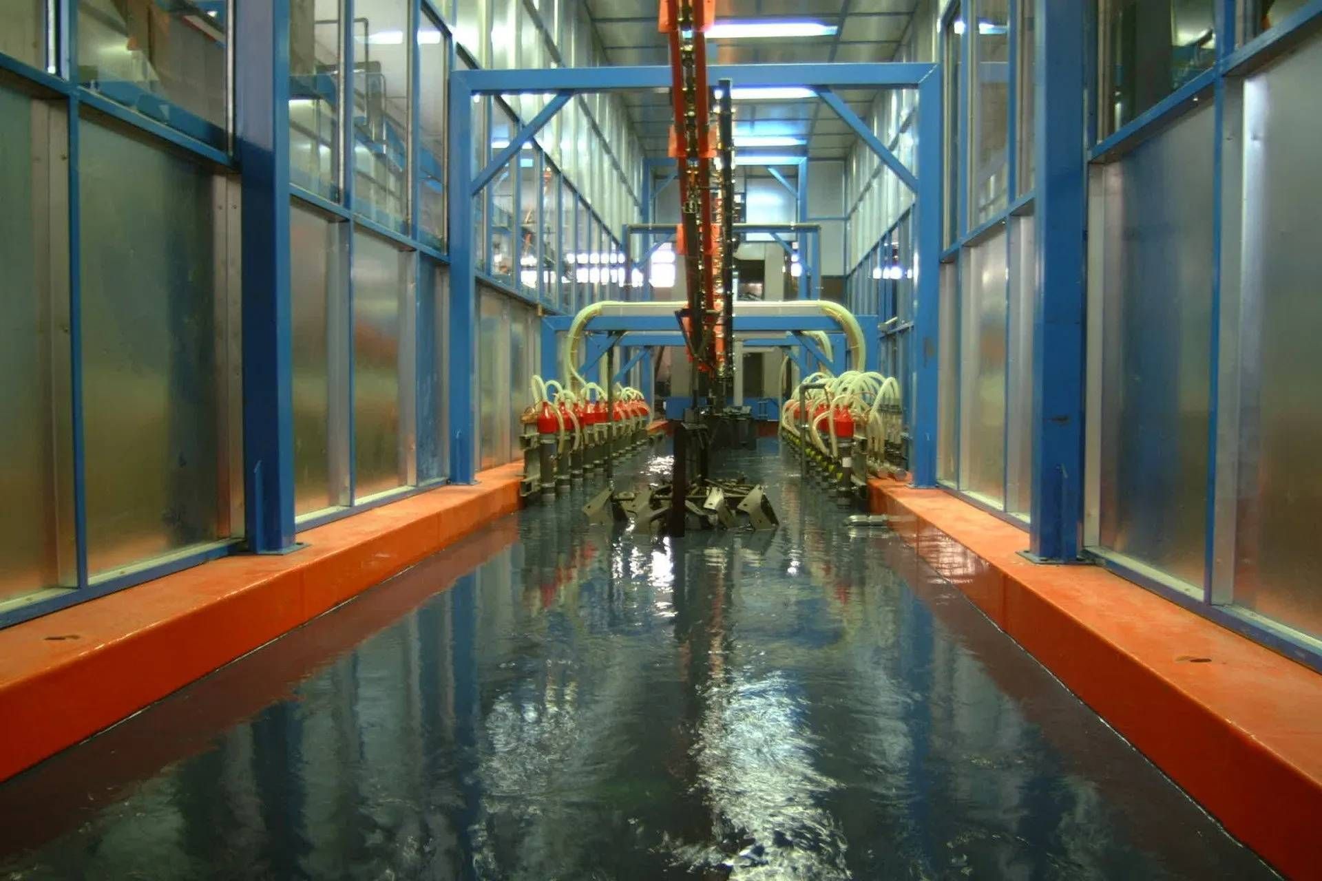 Impianto industriale con strutture metalliche blu e arancioni. Pavimenti, macchinari e tubazioni riflettenti.
