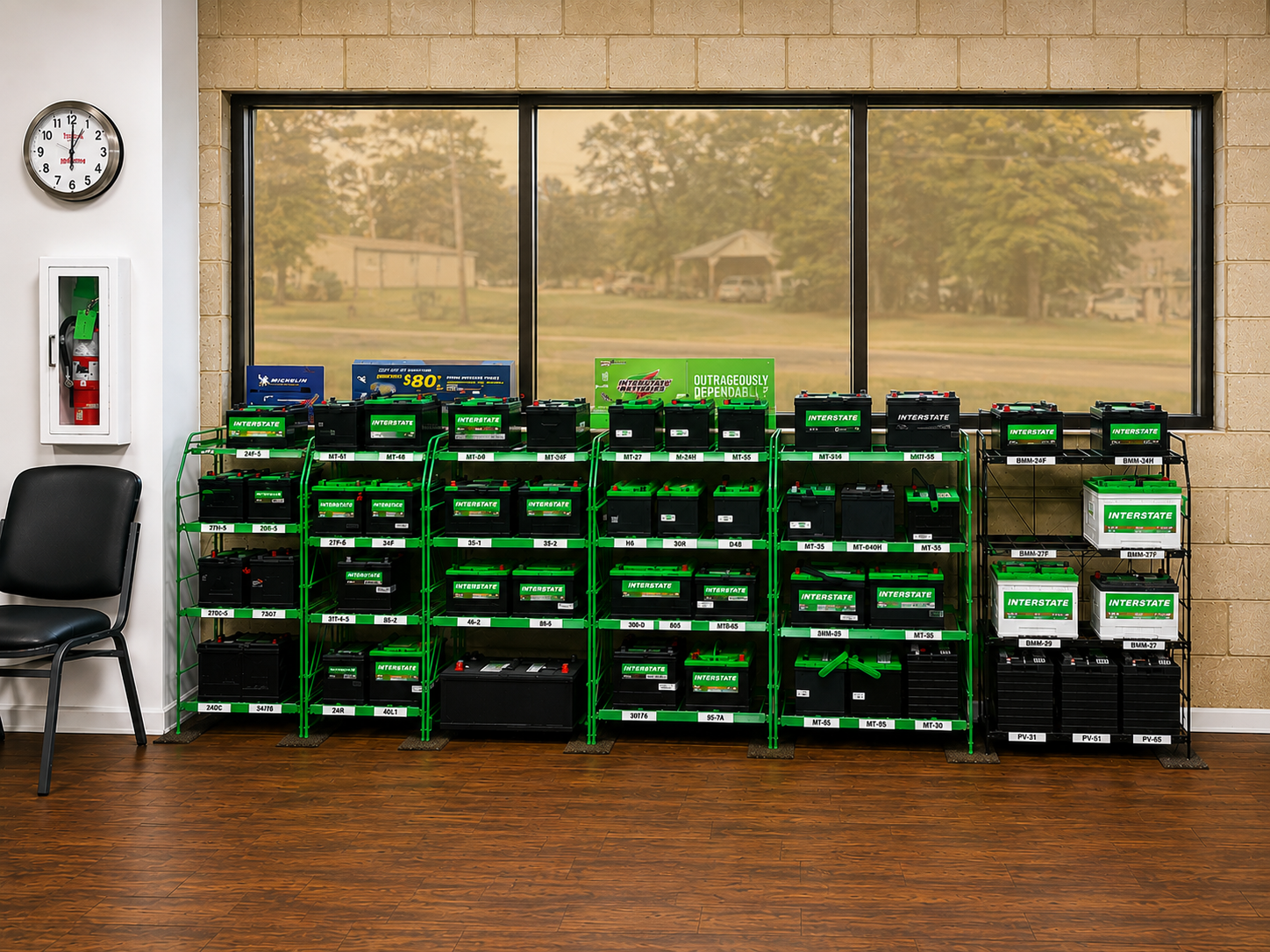 Stacks of black-and-green batteries against a windowed wall in a room with a chair and clock.