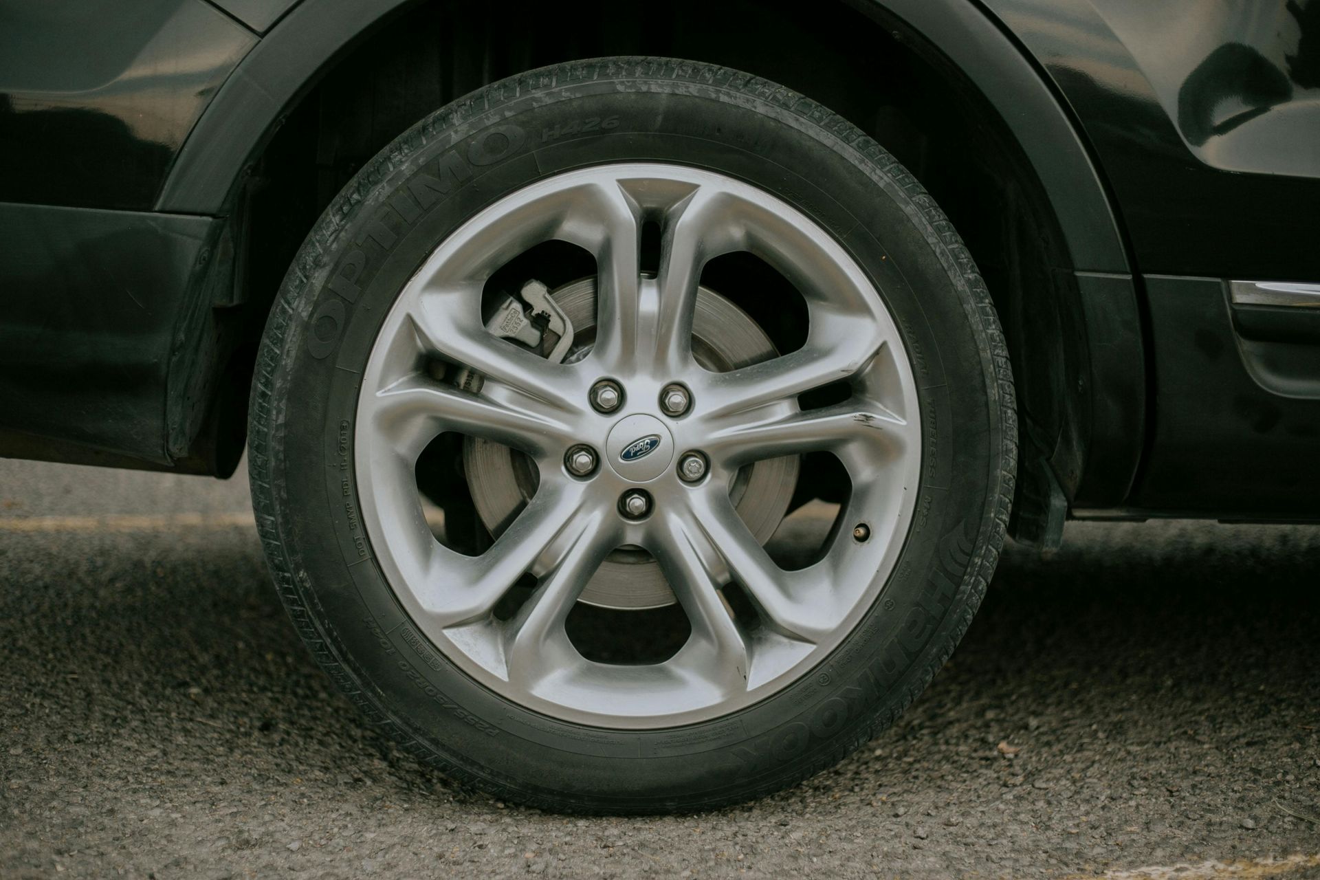 Close-up of a silver car wheel and tire on a black SUV, parked on pavement.