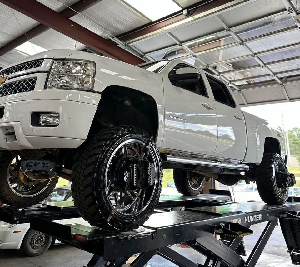 White lifted pickup truck on a car lift in a garage, with large black wheels and off-road tires