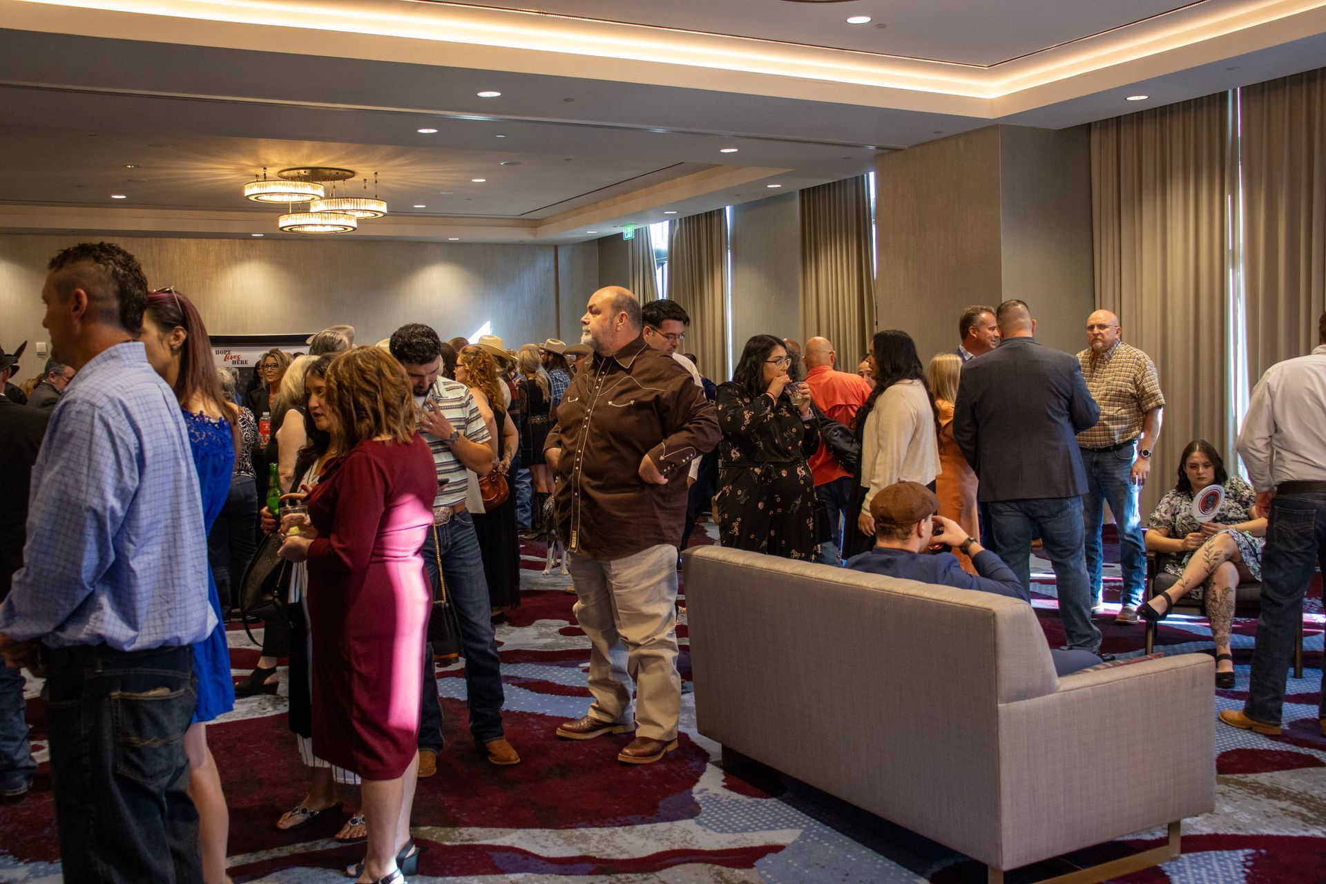 A diverse group of people gathers in a well-lit hotel ballroom for a social or networking event.