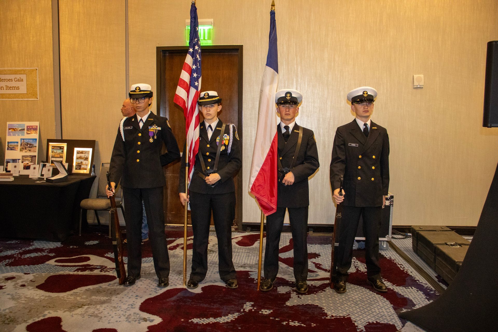 Four individuals in Navy-style uniforms stand in a line, holding a U.S. flag and a French flag indoors.