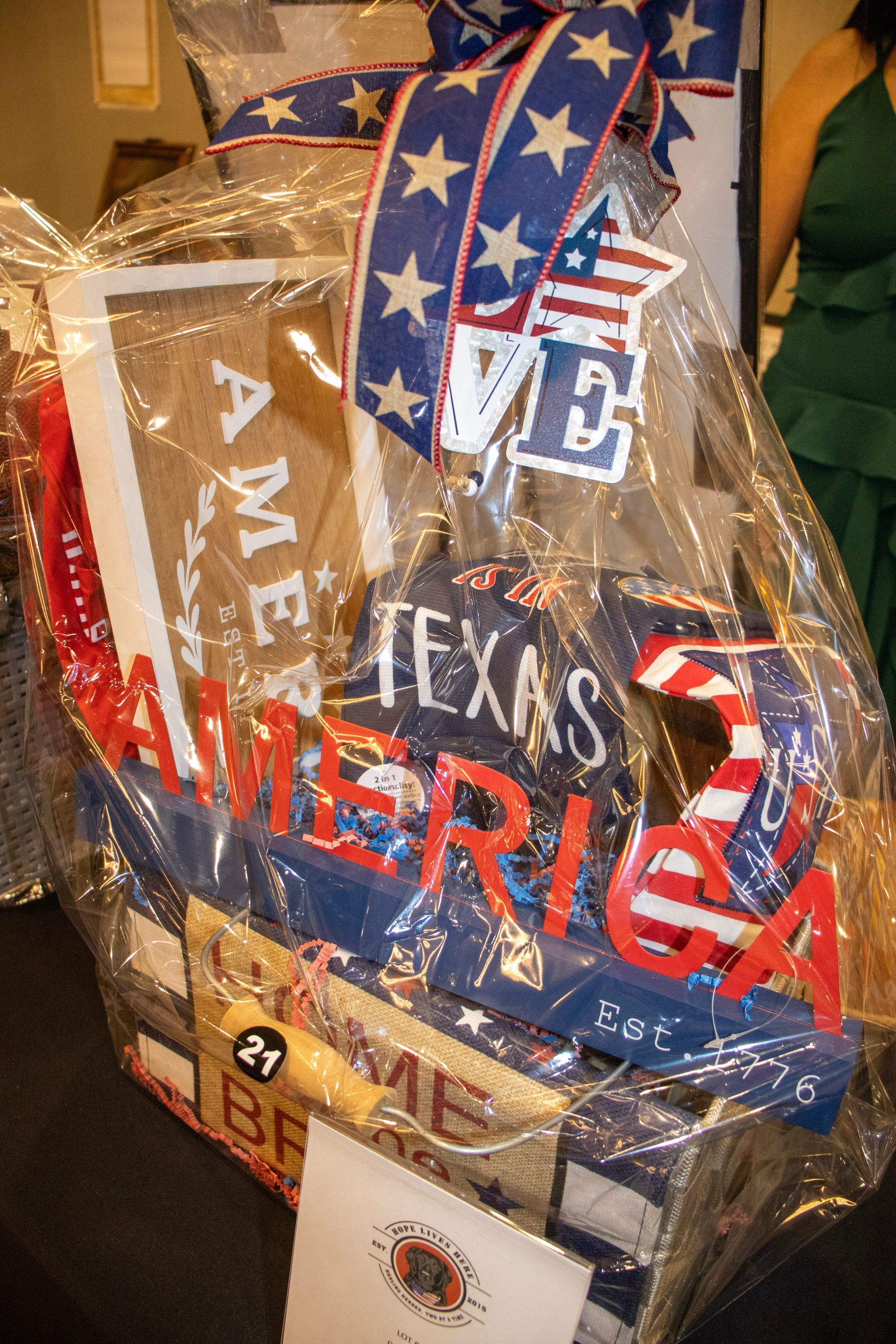 A gift basket wrapped in clear plastic, featuring patriotic-themed decor, including a 