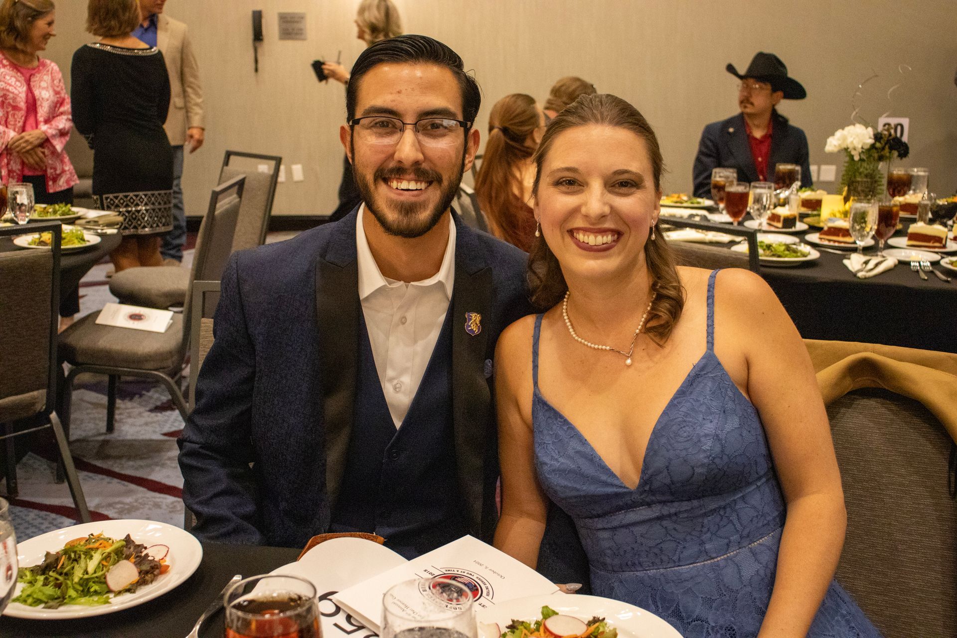 A smiling couple posing for a photo at a banquet table in a dimly lit event space.