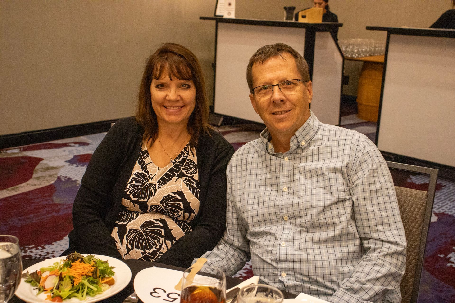 A smiling couple sits at a table with a salad in a restaurant setting.