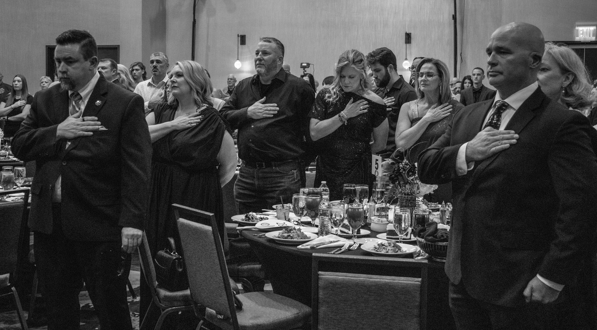 A group of people standing at a formal event, hands over their hearts as if reciting the Pledge of Allegiance.