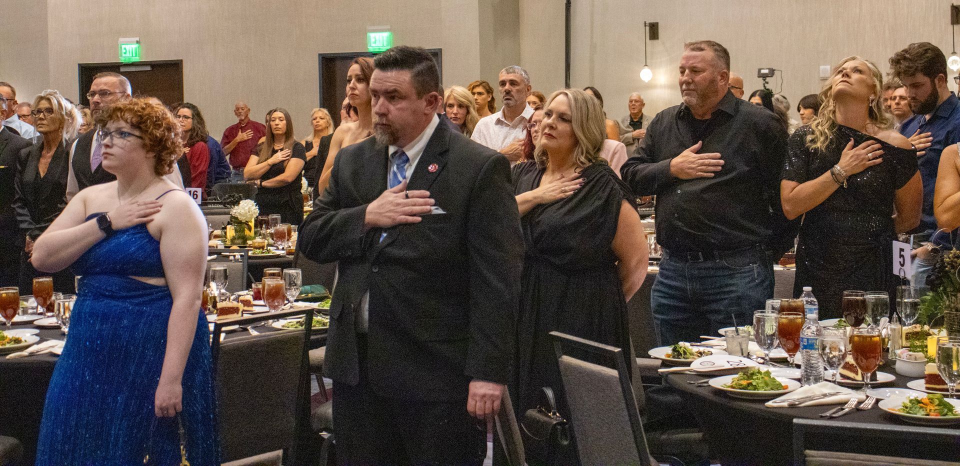 A group of people standing in a formal room with their hands over their hearts, facing forward during a solemn ceremony.