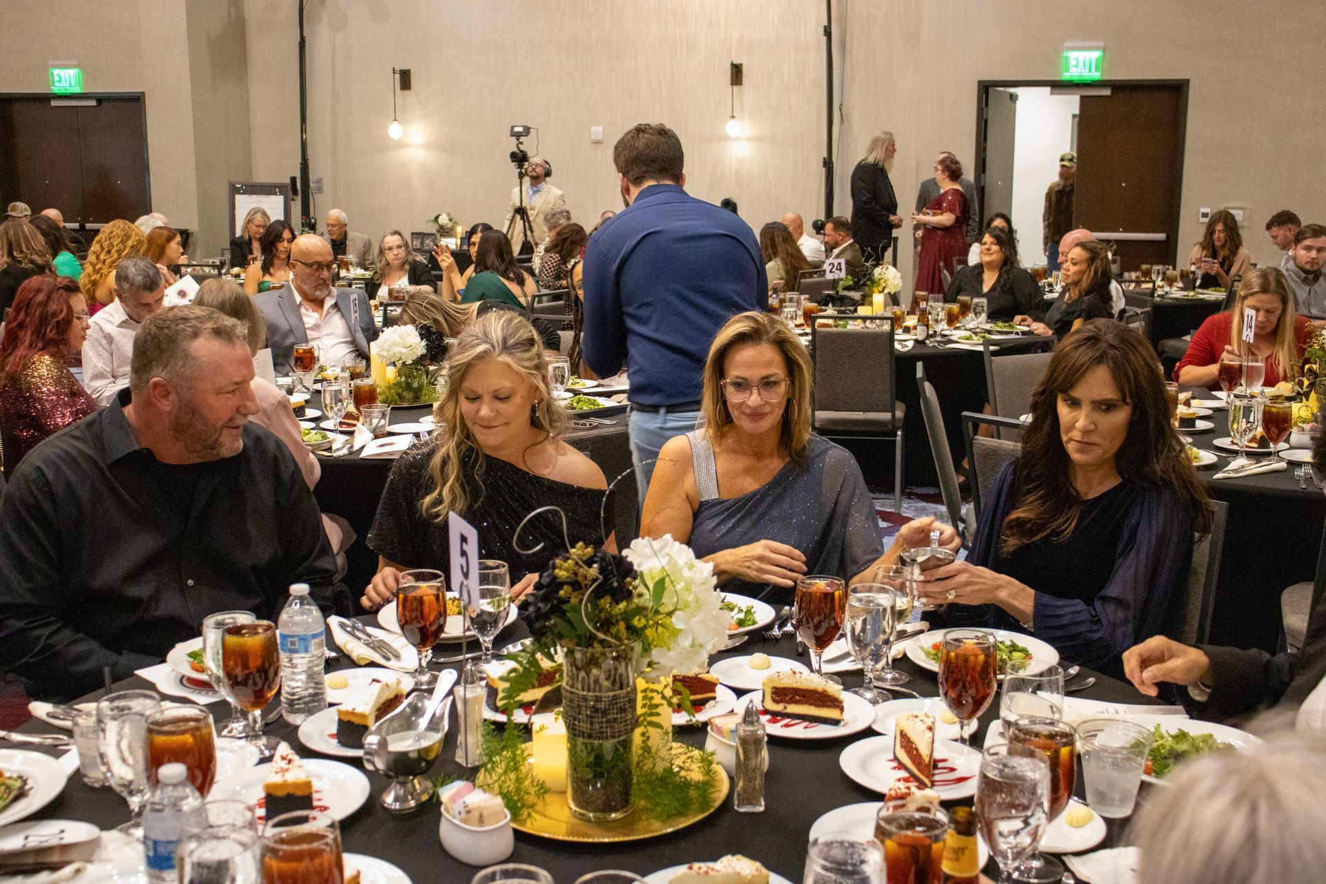 People sit at round tables in a banquet hall, enjoying a meal and socializing during a formal event.