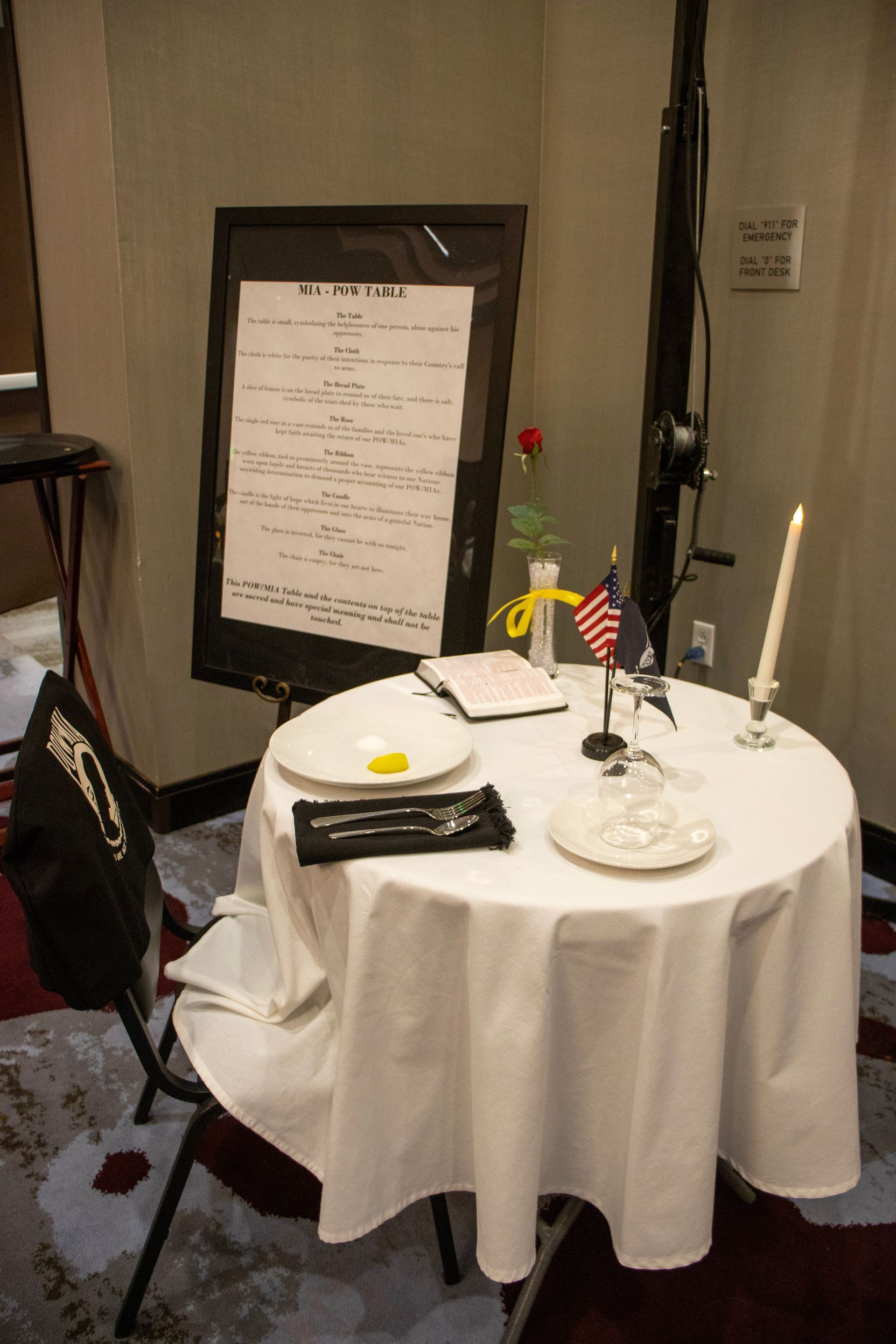 A ceremonial POW/MIA Missing Man table with a single setting, a white rose, a candle, and a memorial explanation sign.