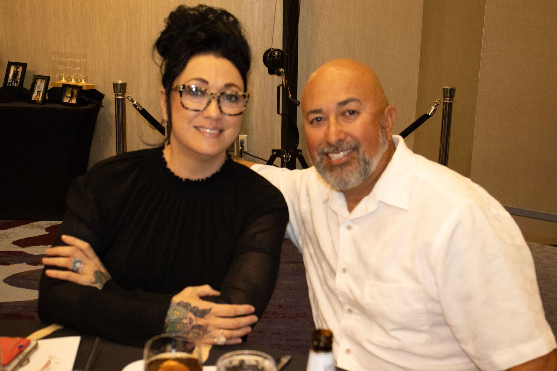 A woman in a black blouse and a man in a white button-down shirt smiling while sitting together at a table.