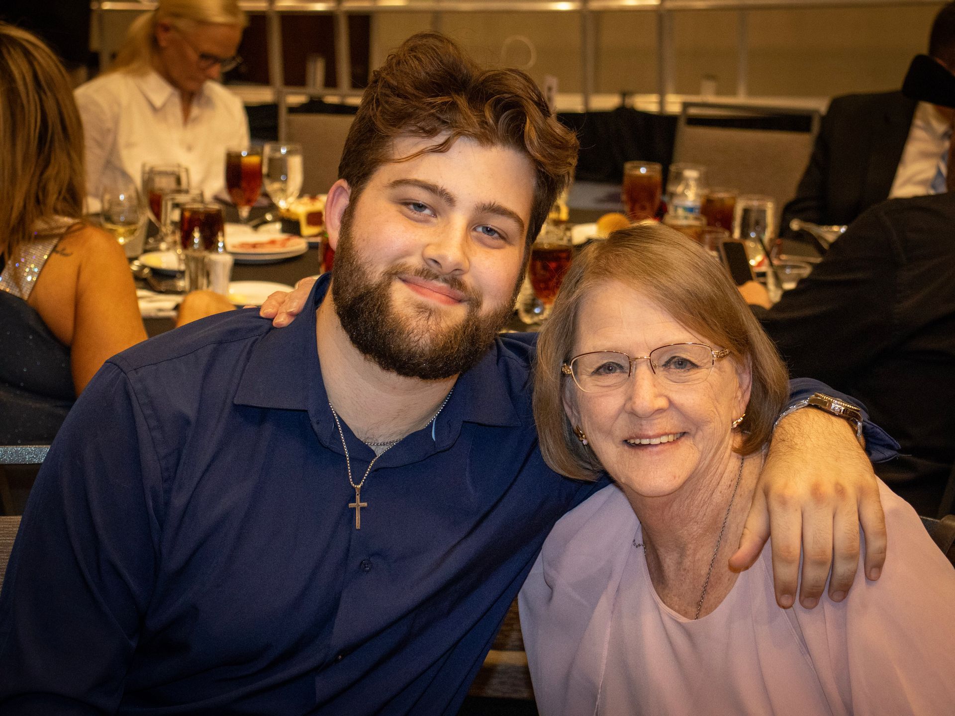 A young man with a beard and a woman smiling, sitting together at a restaurant table, his arm around her shoulders.