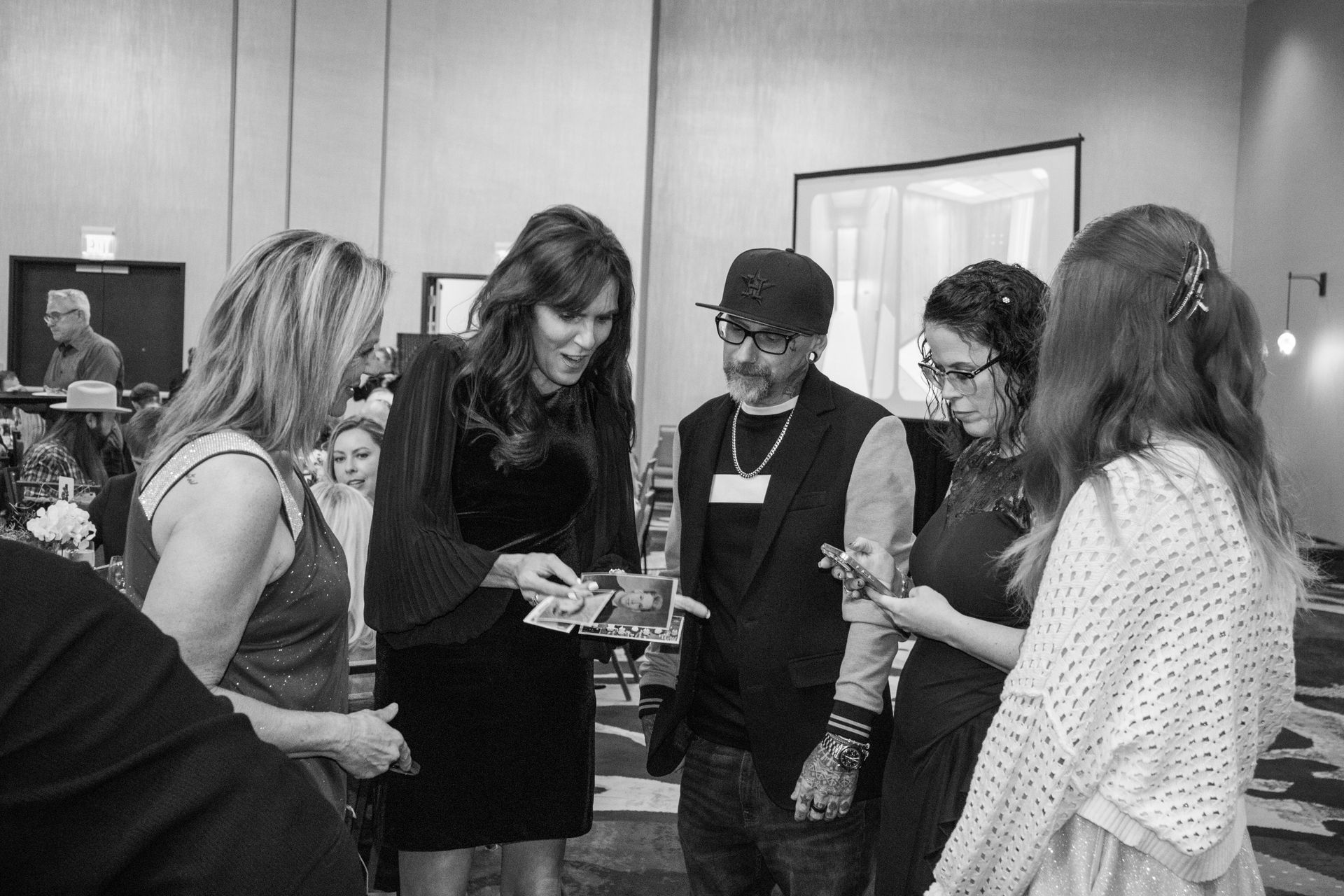 Four people stand in a room, focused on a document one person holds, while others observe and interact in a group setting.
