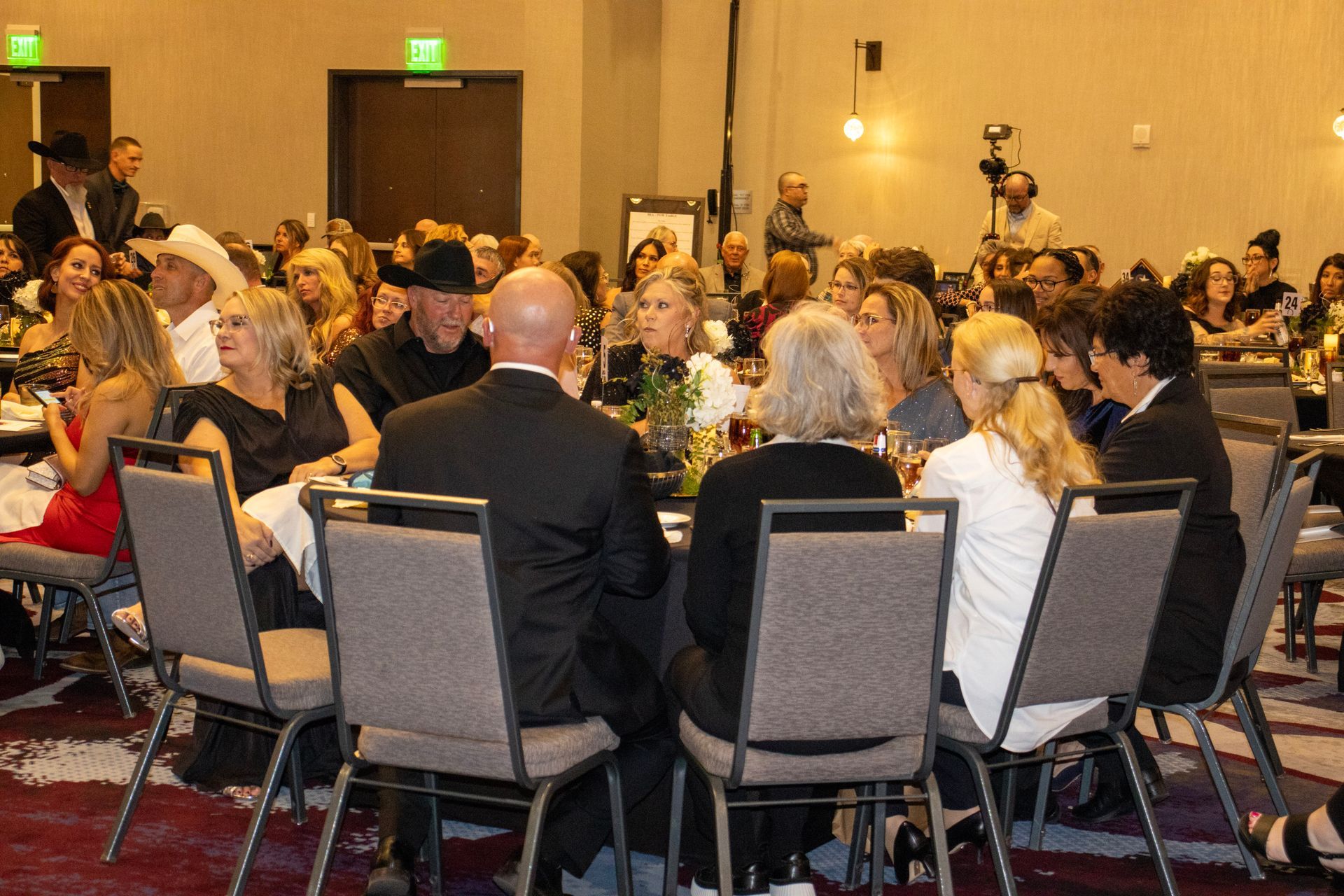 People seated at round tables in a banquet hall, attending a professional event or formal dinner.