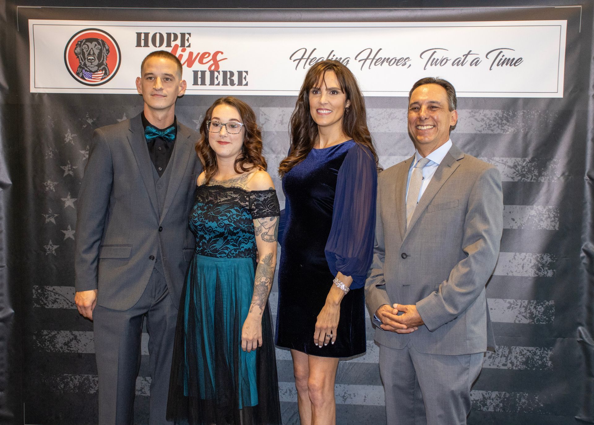 Four people standing in formal attire in front of a banner that reads, 