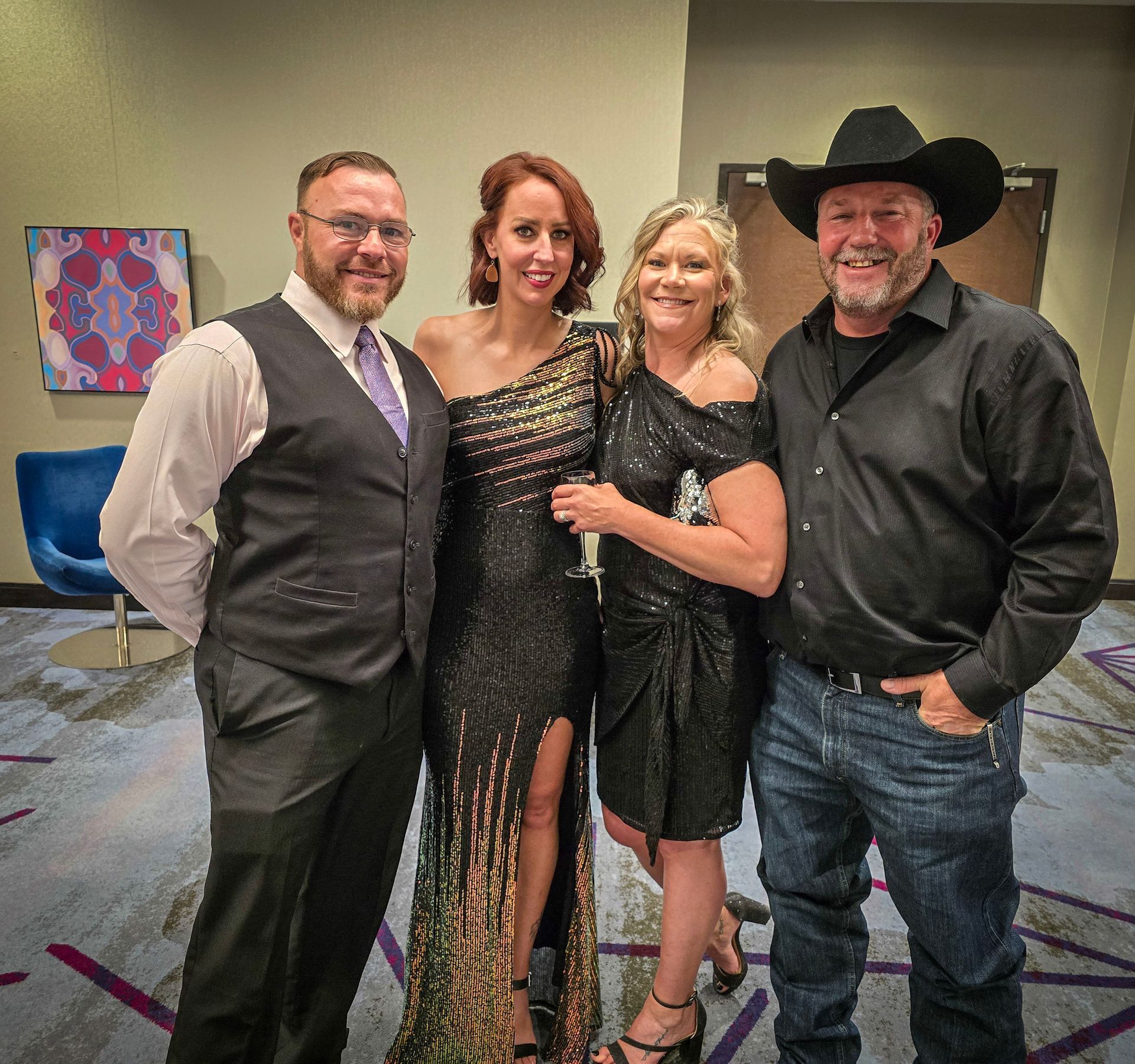 Four people stand together in a formal setting, dressed in evening wear and a western-style shirt and cowboy hat.