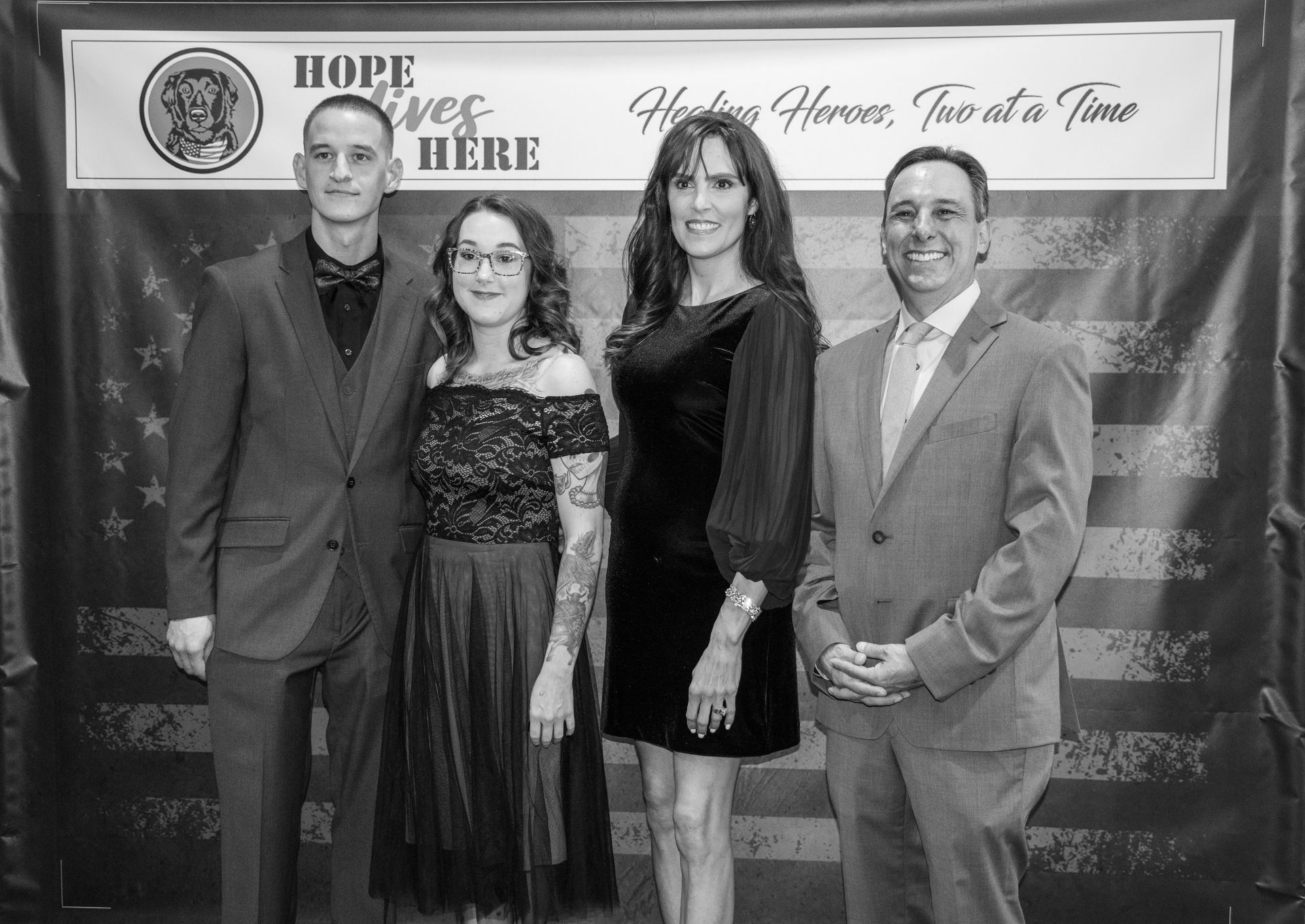Four people pose in formal attire in front of a backdrop that reads 