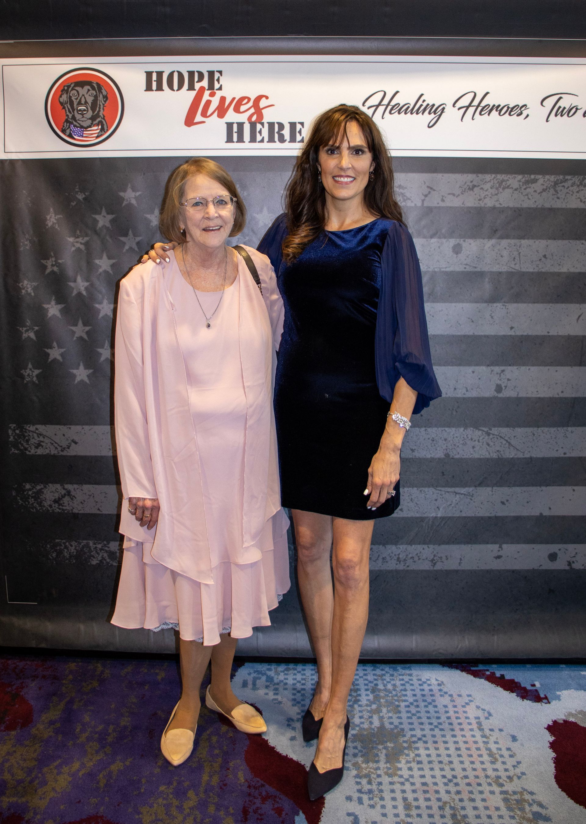 Two people stand together smiling in front of a banner that reads 