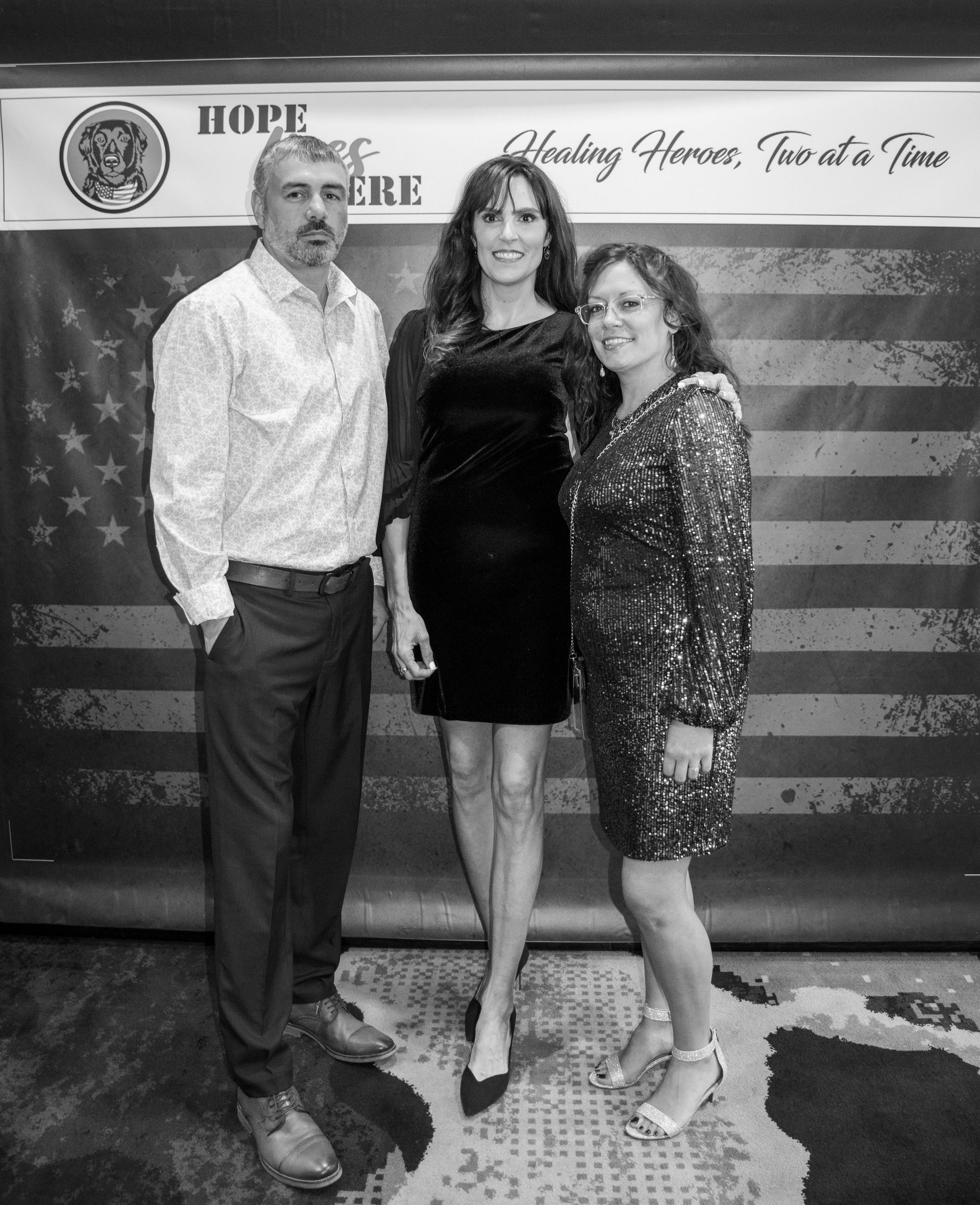 Three people pose for a photo in front of a backdrop featuring an American flag and the text “Healing Heroes, One at a Time.”