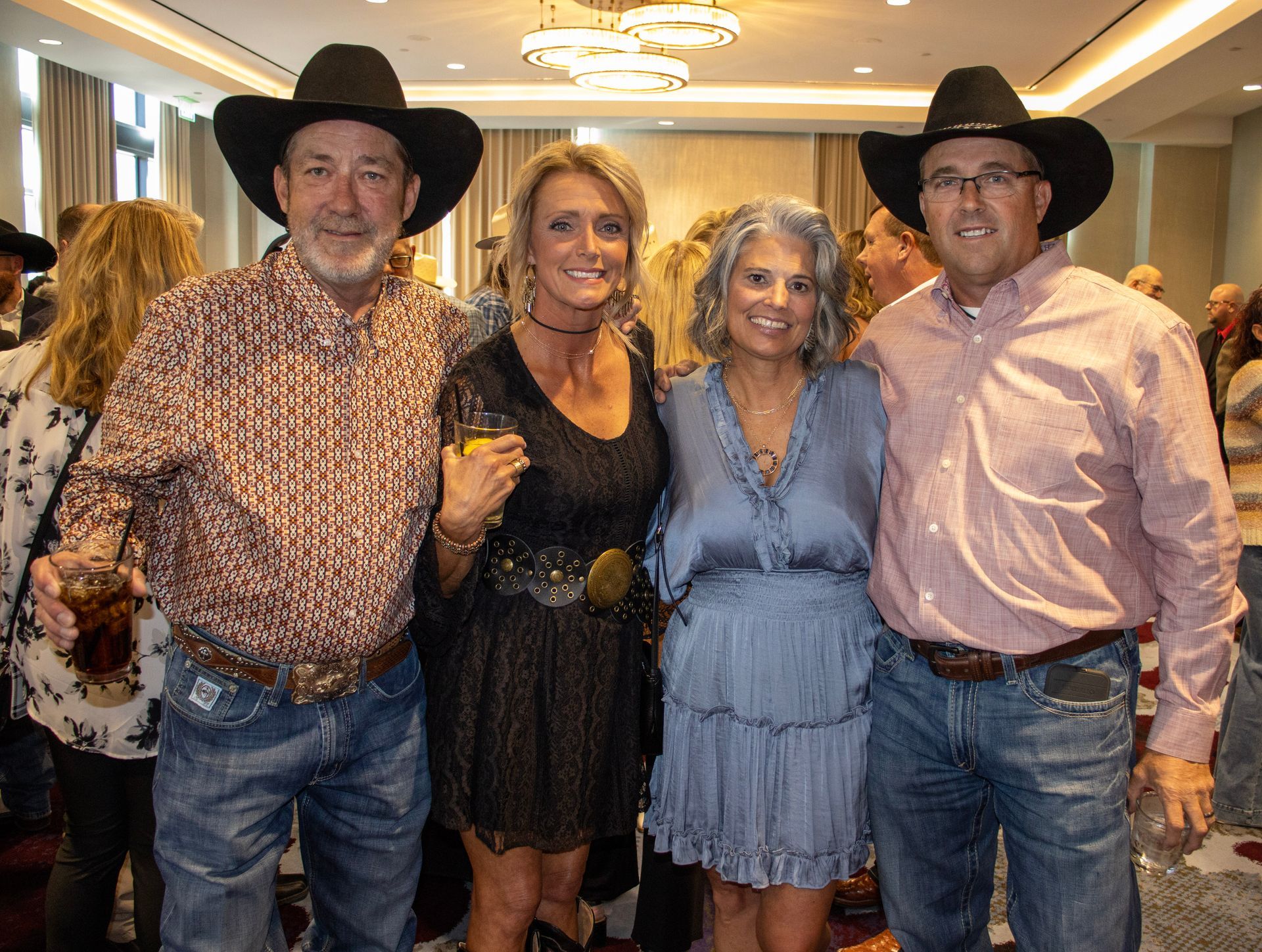 Four people stand together in a room, two wearing cowboy hats, posed for a photo at an indoor event.