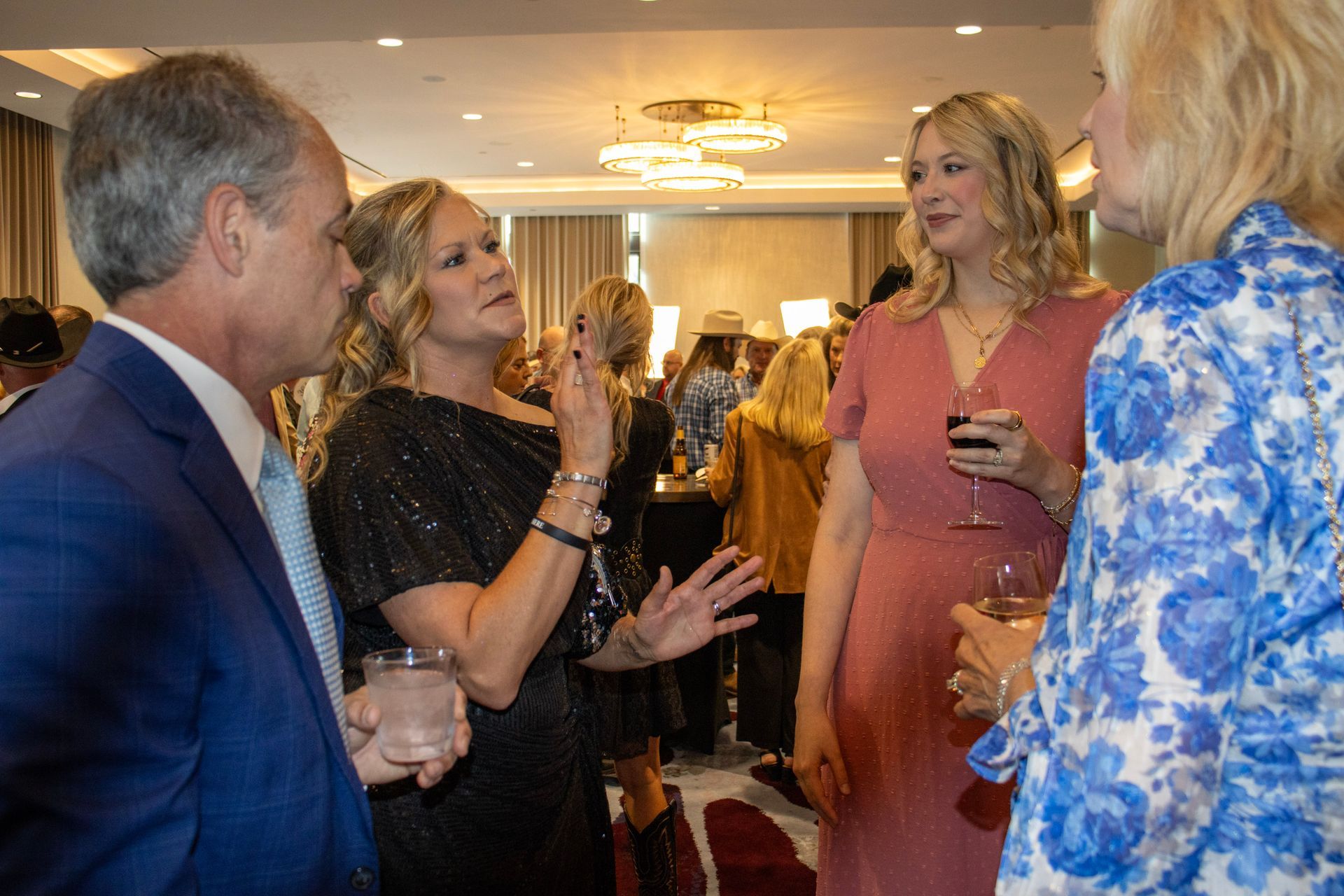 A group of people dressed in formal attire conversing and holding drinks at an indoor social event.