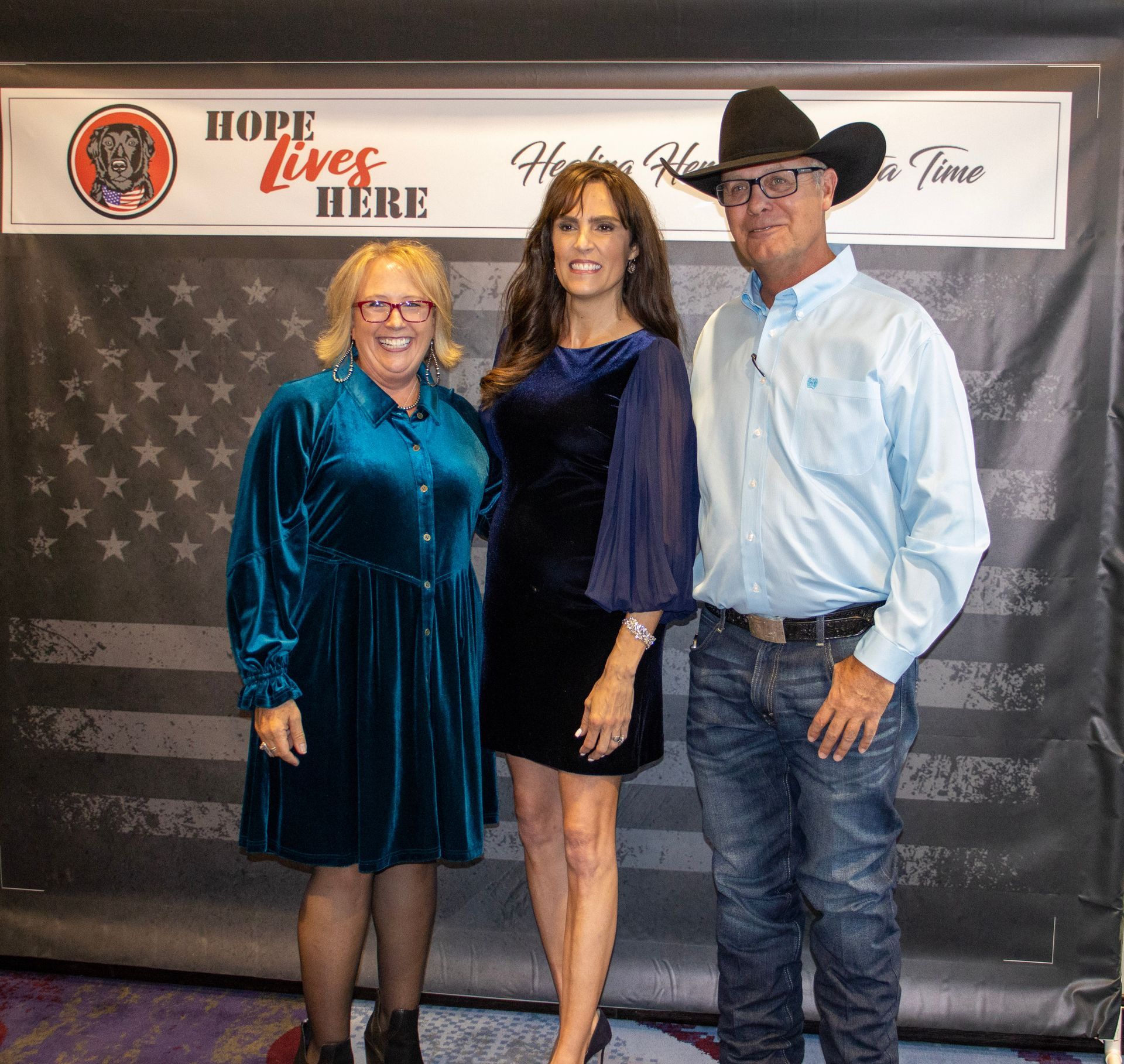 Three people stand smiling in front of a banner that reads 