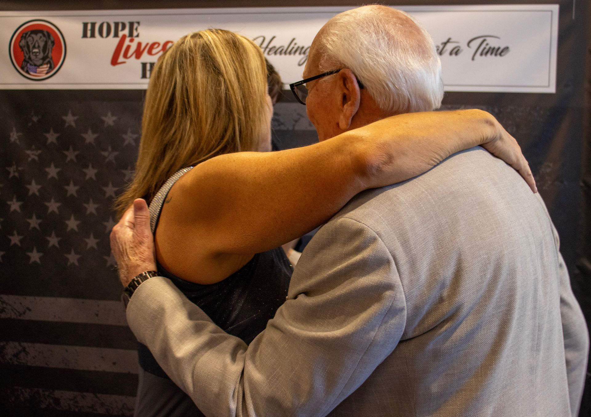 Two people embrace in front of a banner that reads, 