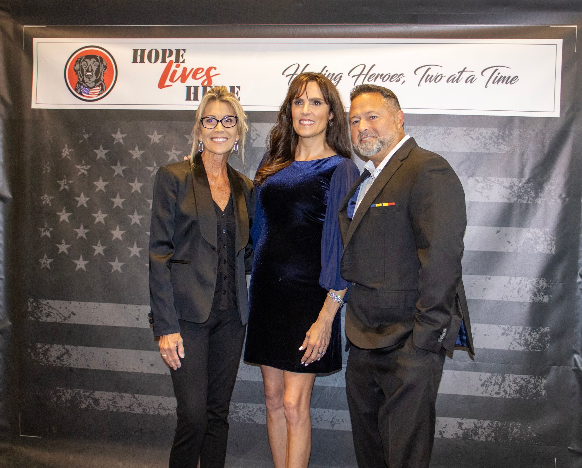 Three people stand smiling for a photo in front of a banner that reads 