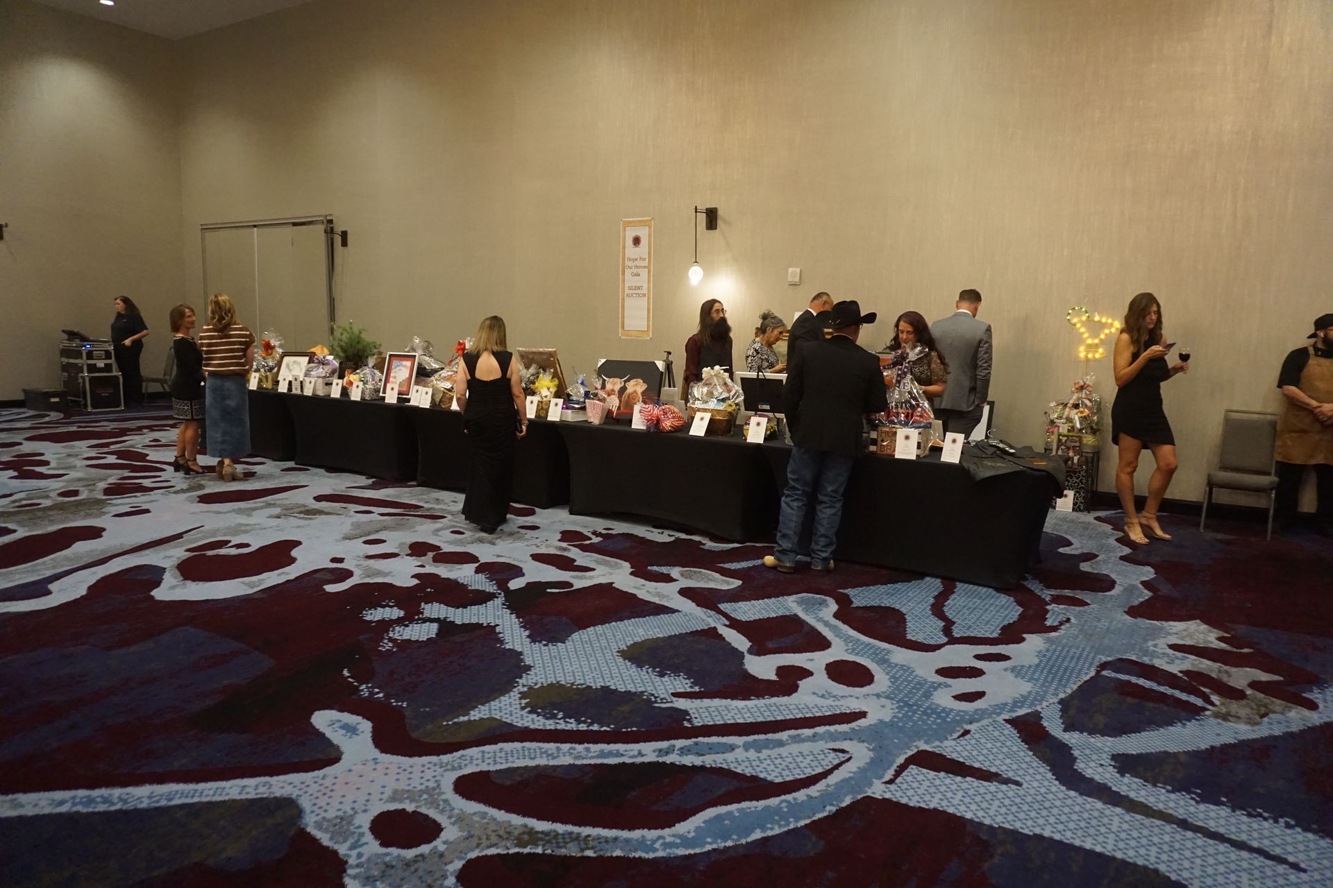 People gather around a long banquet table with displays in a conference room with patterned carpet and beige walls.
