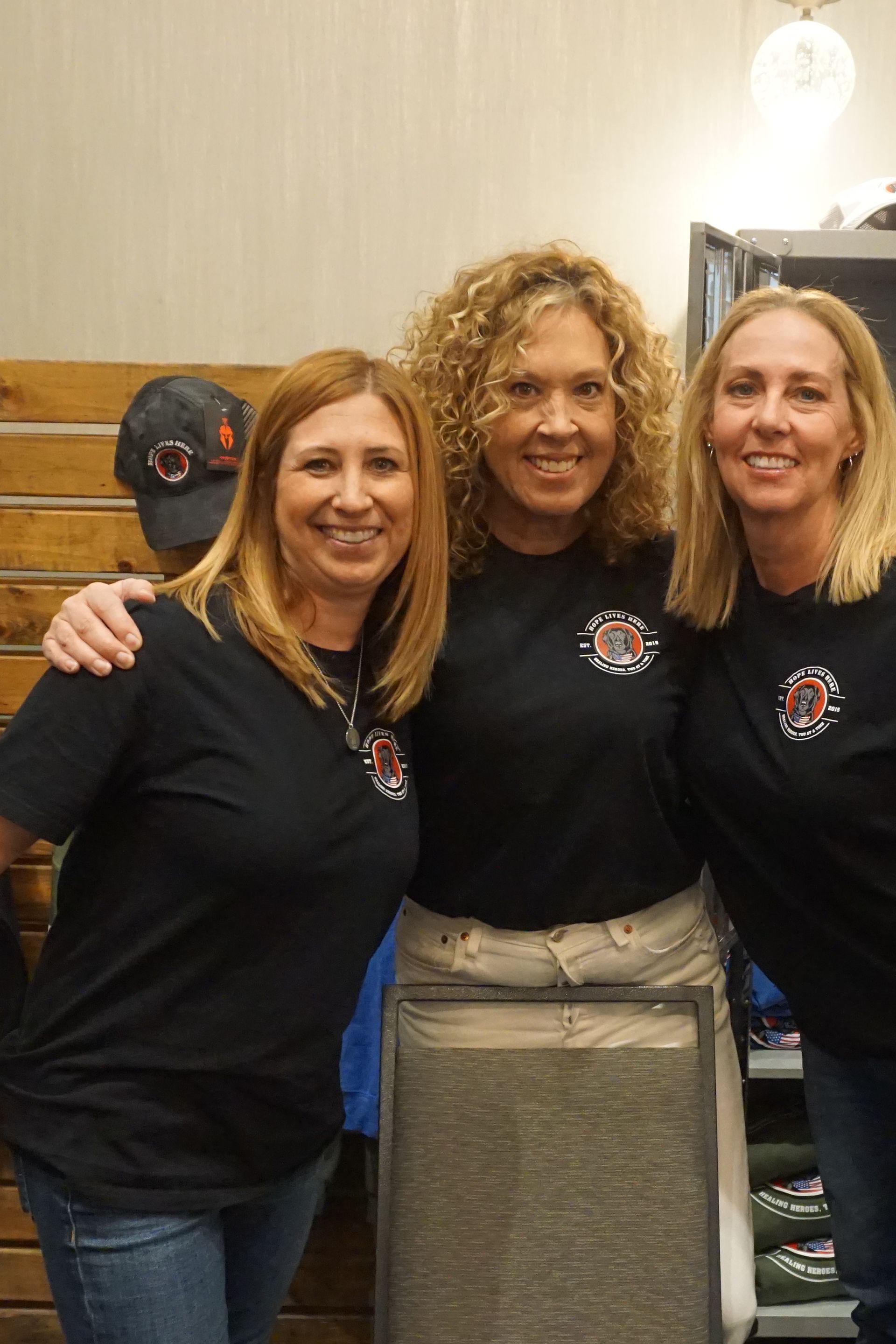 Three people stand side-by-side wearing matching navy blue t-shirts with a circular logo, smiling at the camera.