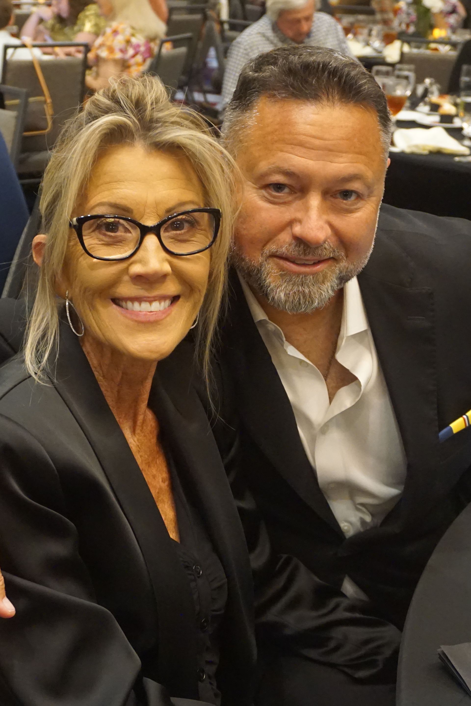 A smiling person with glasses and a person with a beard posing together at an indoor dinner event.