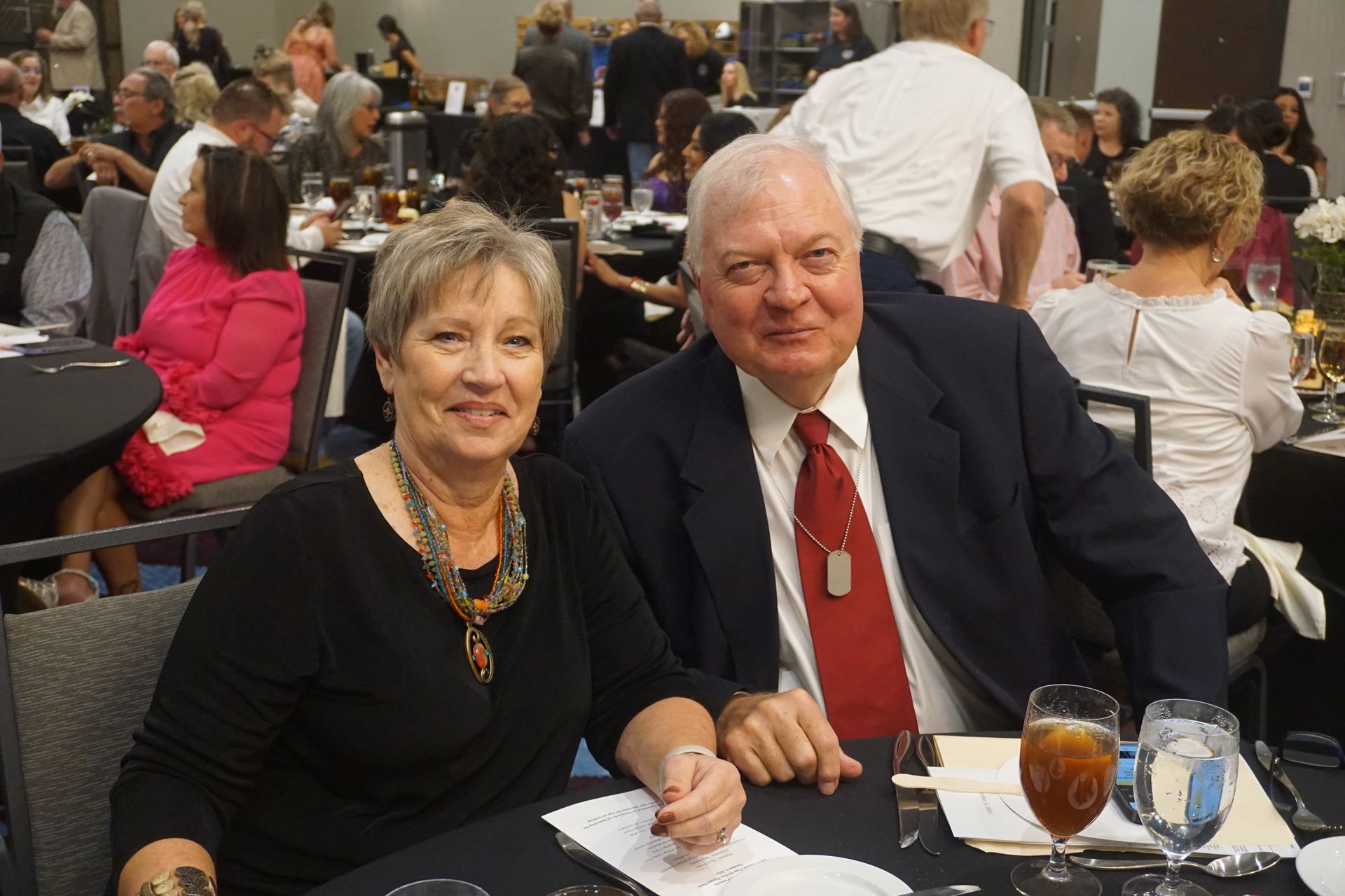 A couple seated at a table during a banquet, posing for a photo in a dimly lit event space.
