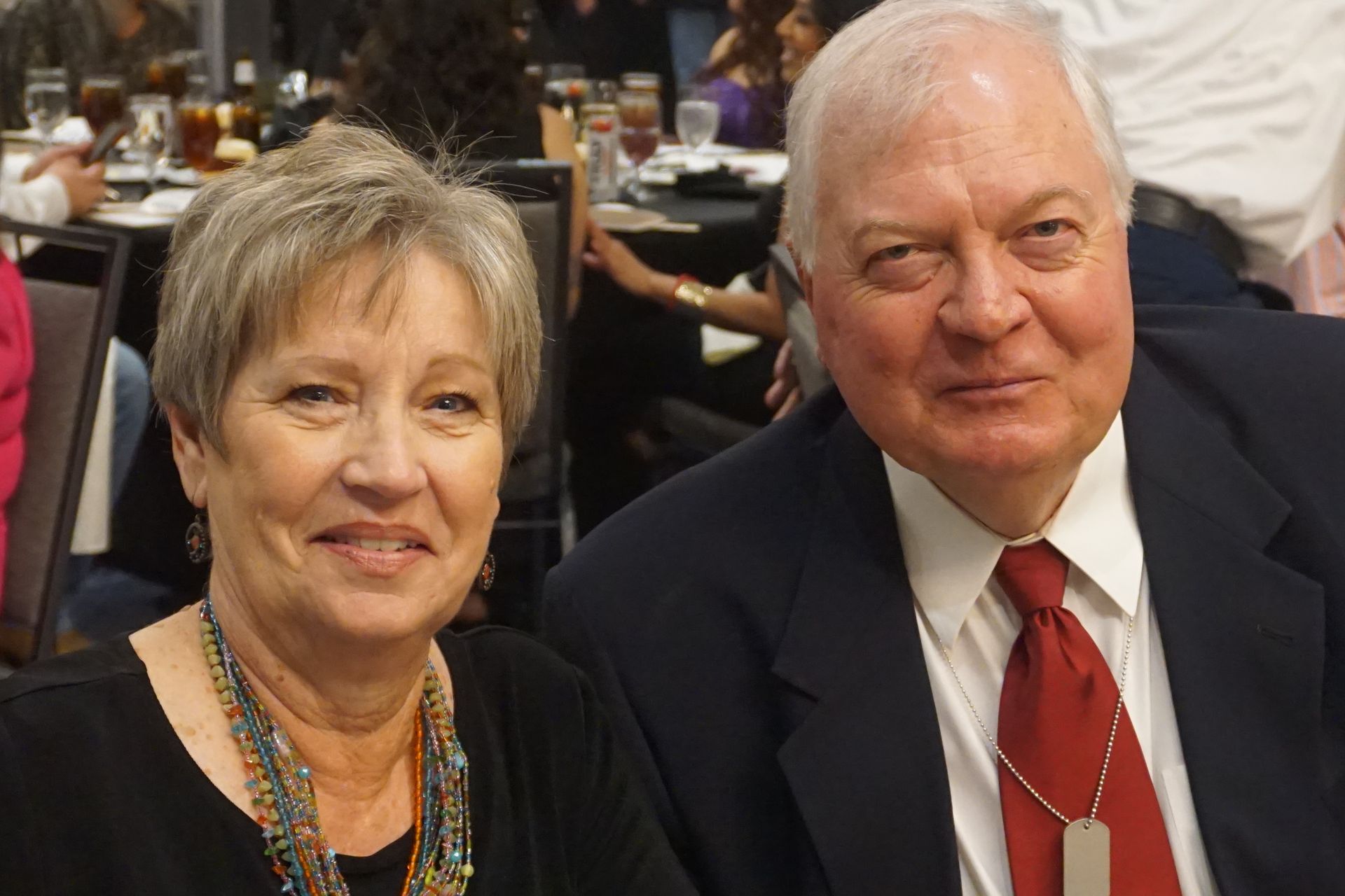 A smiling couple in formal attire pose together at a banquet table.