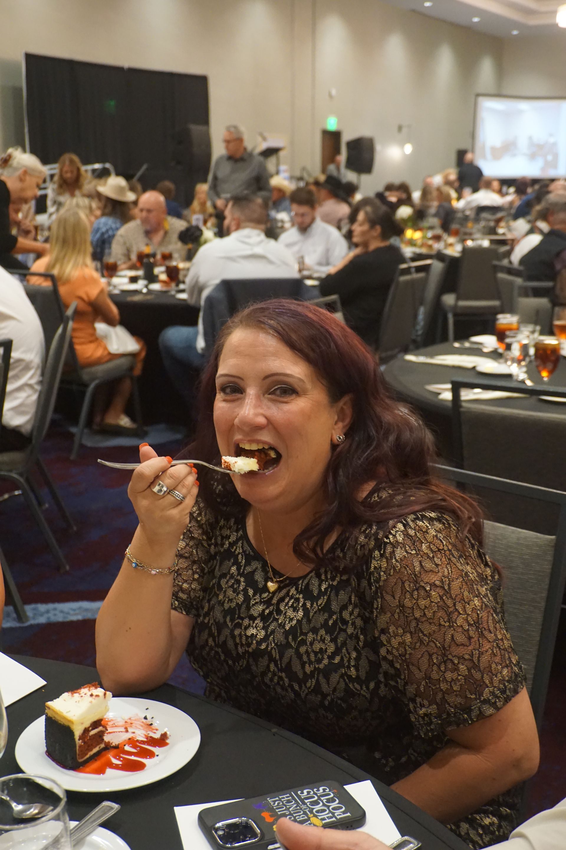 A person eating cake at a table in a crowded banquet hall.