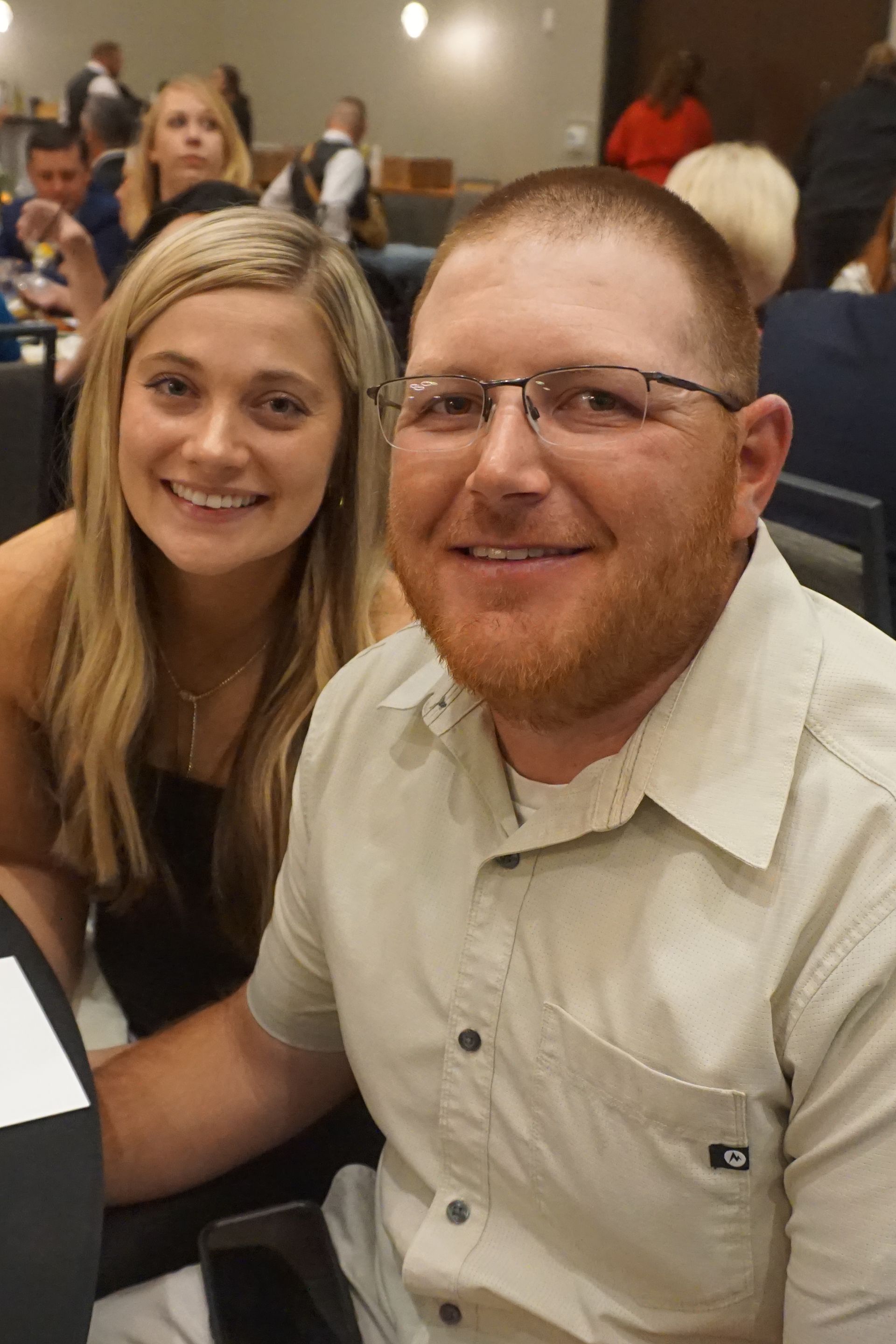 A couple smiles while sitting together at a table in a dimly lit event space.