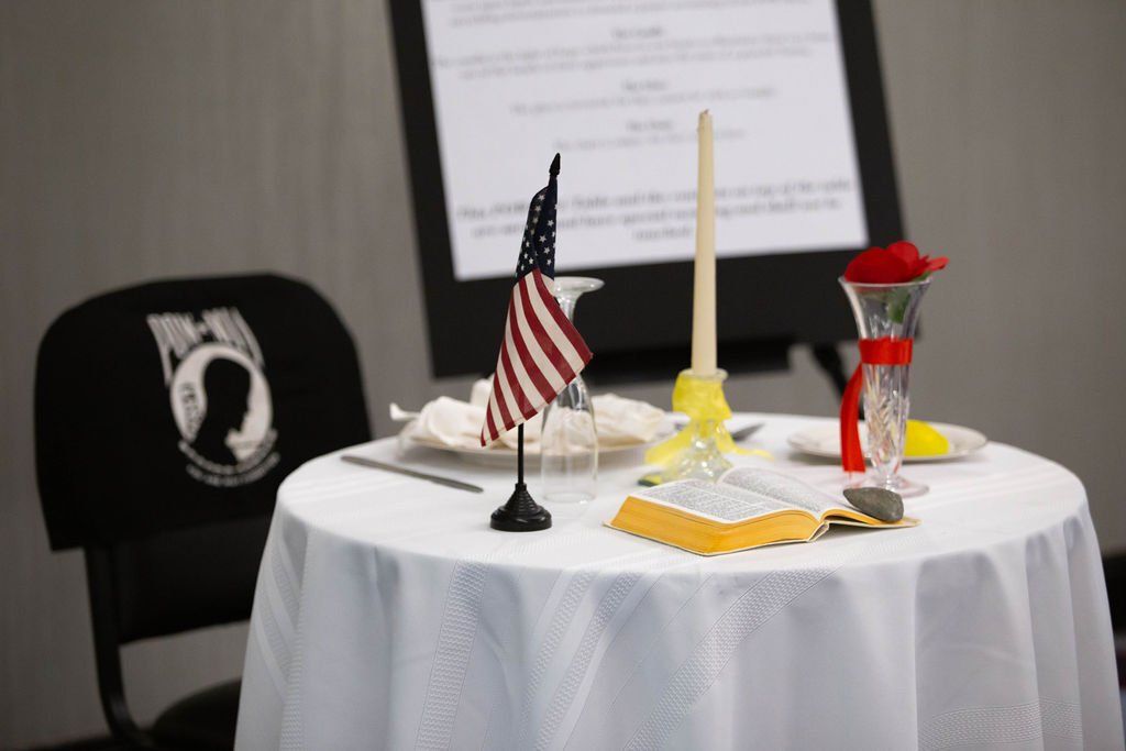 A Missing Man table with a white cloth, a single place setting, a candle, an American flag, and a chair with a POW-MIA logo.