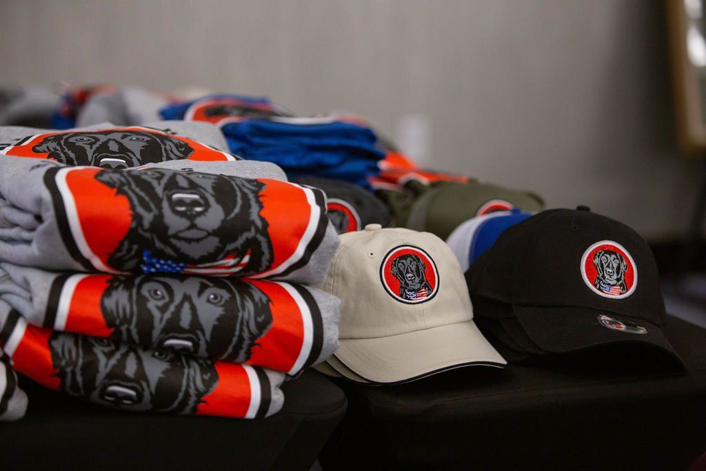 A table displays stacks of grey sweatshirts with bear graphics alongside tan and black baseball caps with matching logos.