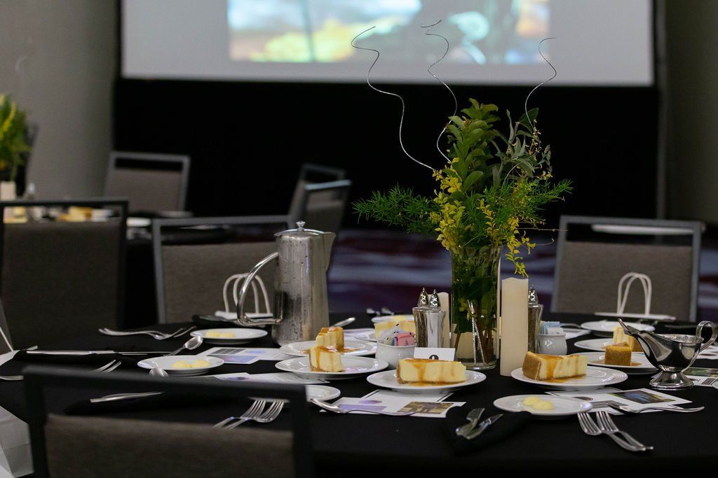 A round table set for a formal event with black tablecloths, floral centerpieces, place settings, and dessert plates.
