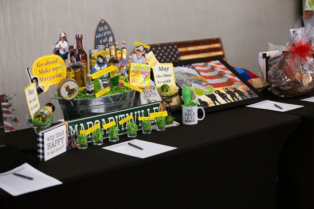 A black tablecloth features two silent auction baskets with patriotic decor, American flags, and signs with pens for bidding.