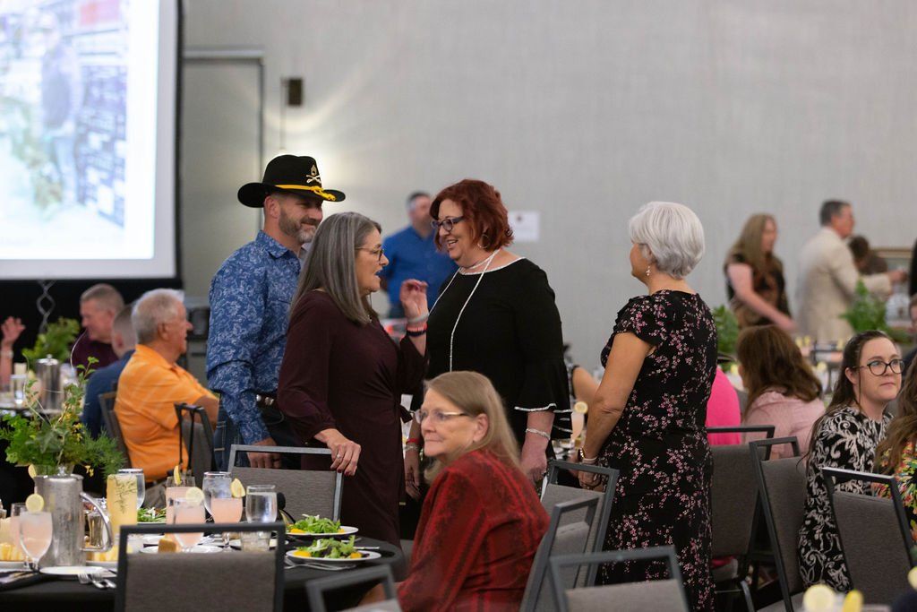 A group of people converse while standing around tables in a brightly lit room, likely at a conference or reception.