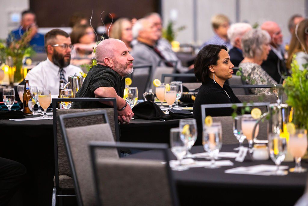 A banquet room with guests at tables during a formal event, focusing on a man and woman seated at a foreground table.