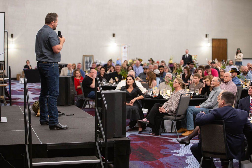 A speaker addresses a large audience seated at tables in a conference room.