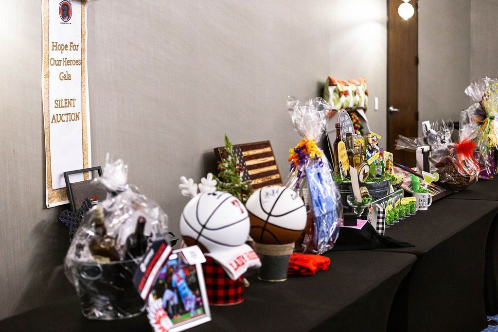 A silent auction table displays various gift baskets and items, including basketball-themed gifts, on a black cloth.