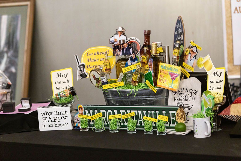 A Margaritaville-themed gift basket set on a black table, featuring alcohol bottles, cocktail signs, and party favors.