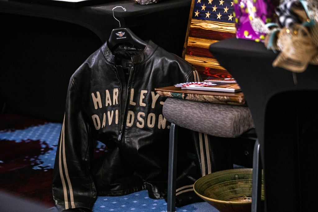 A black Harley-Davidson leather jacket hangs on a chair next to an American flag and a decorative bowl.