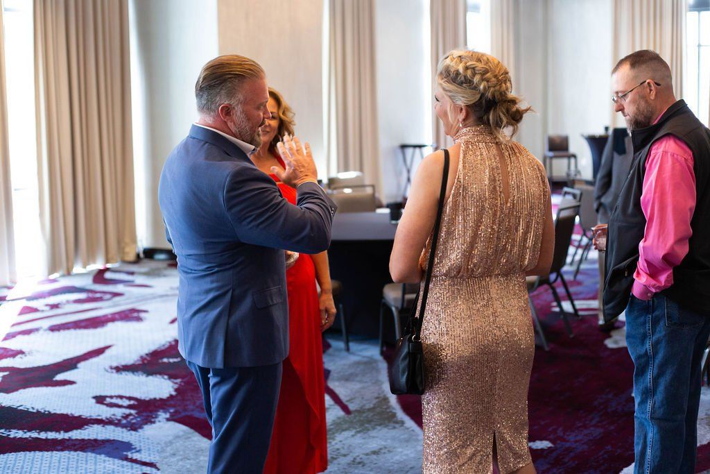 Four people stand in a hotel ballroom with patterned carpeting, engaging in conversation.